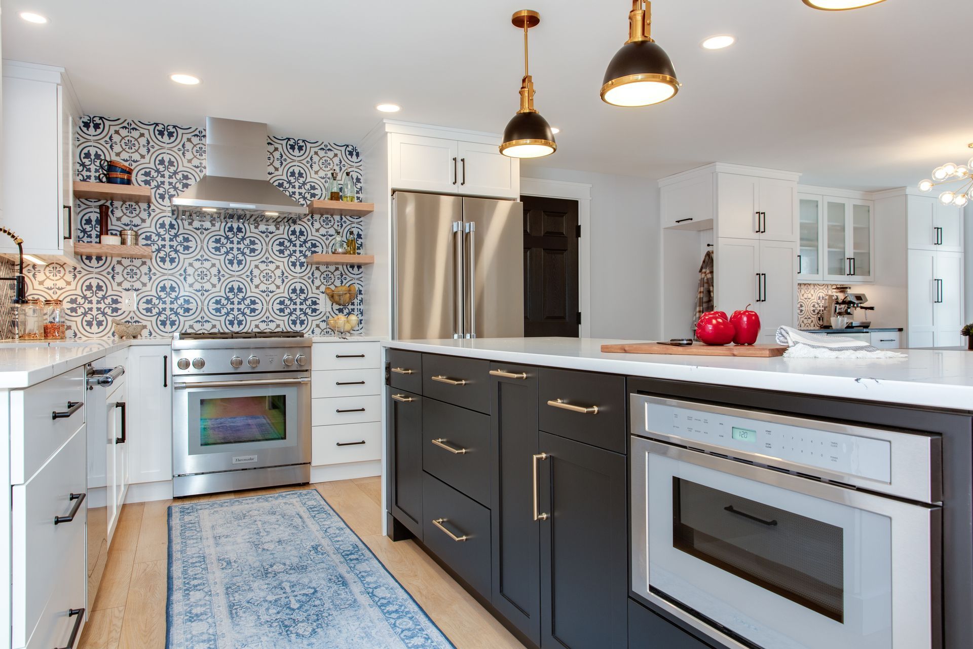 Modern white kitchen with gray island, pendant lights, stainless appliances, and blue mosaic backsplash
