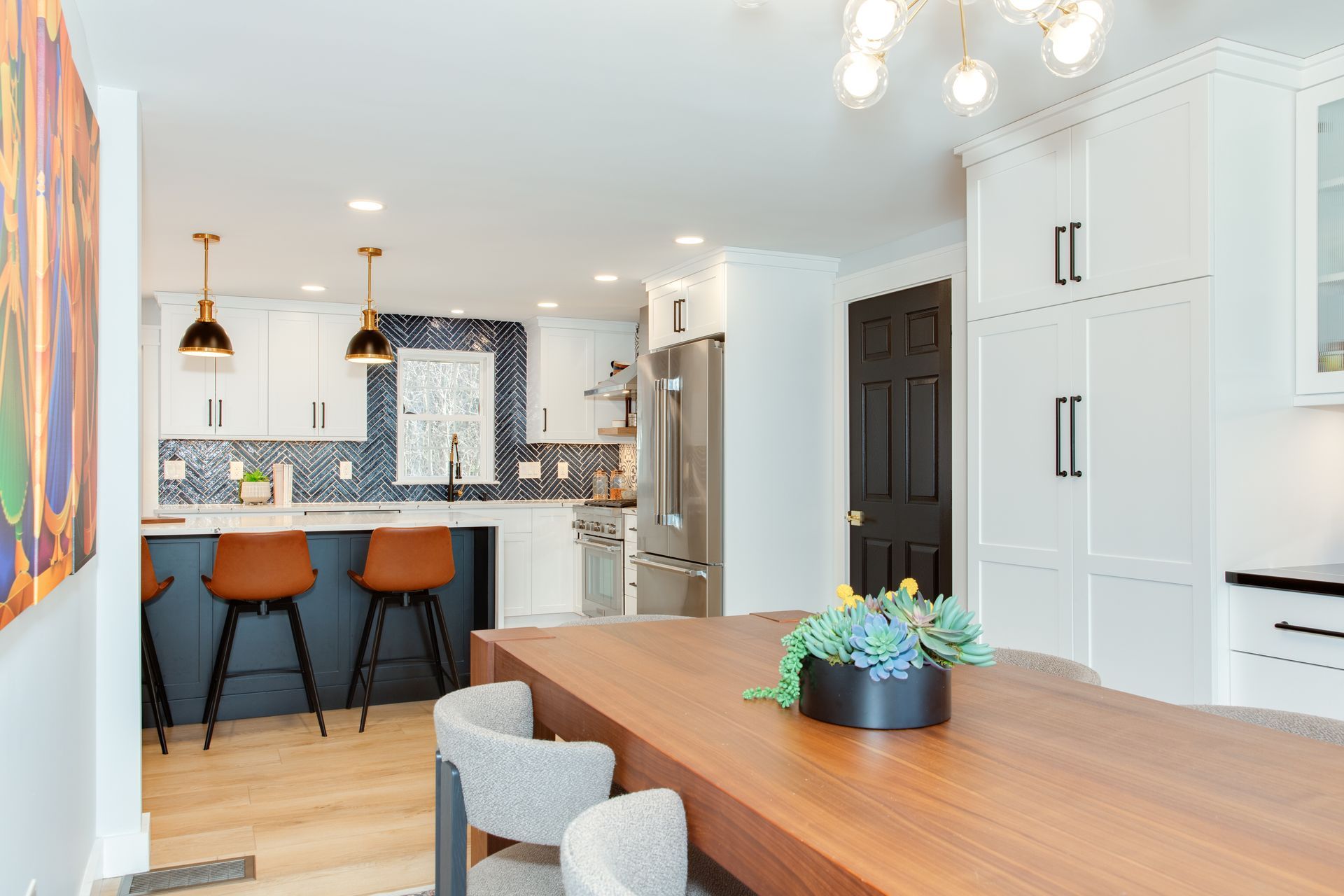 Bright modern kitchen and dining area with white cabinets, blue island, and wooden table.