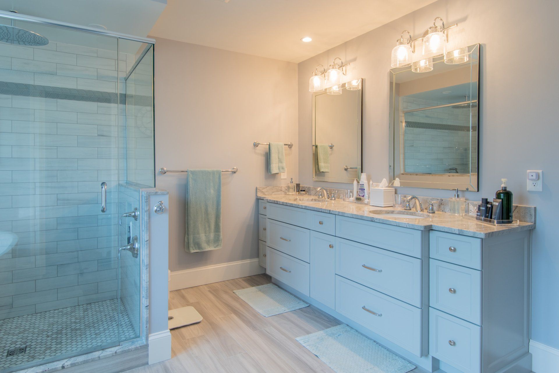 Modern bathroom with glass shower, double vanity, large mirrors, and white tile floors