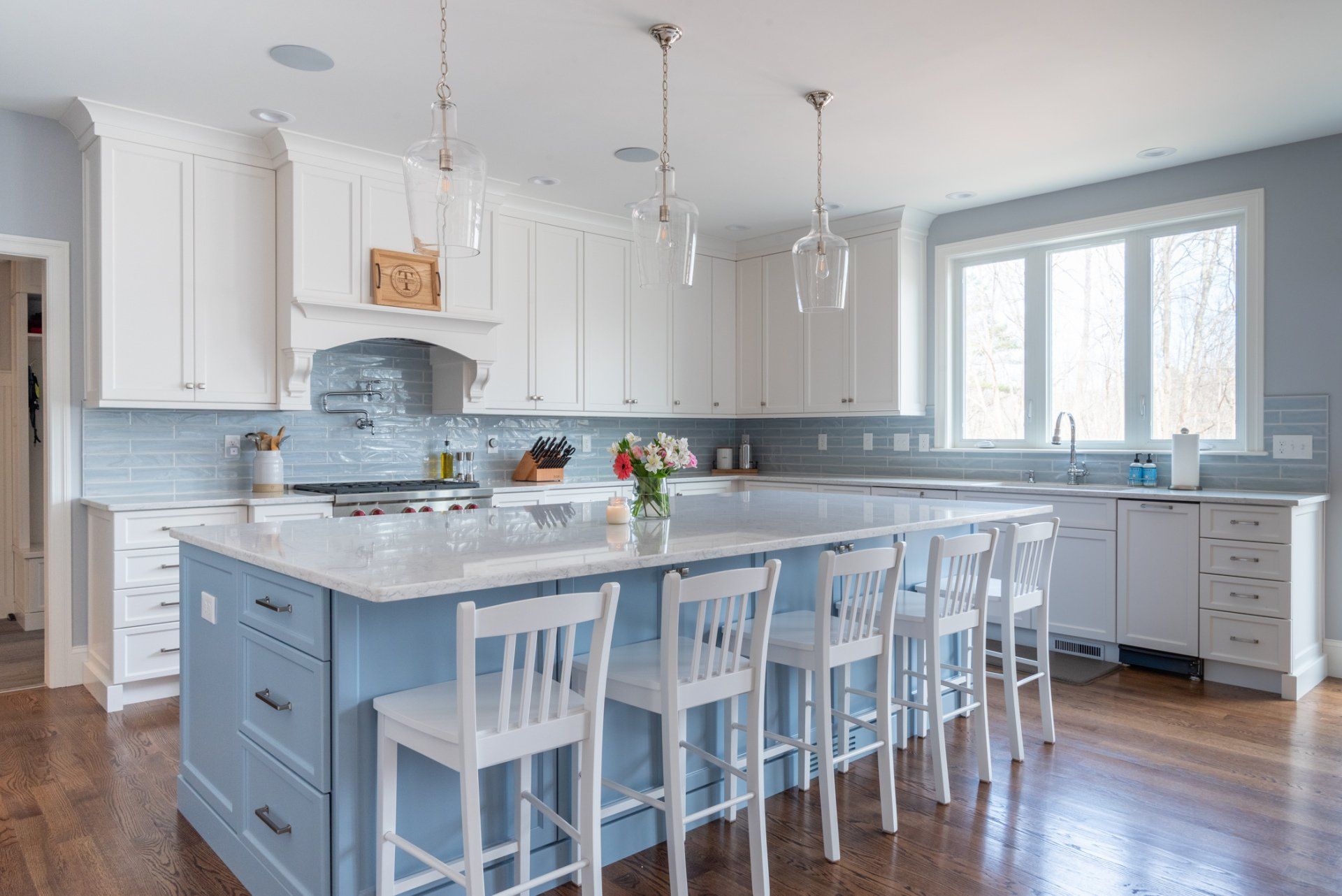 Bright modern kitchen with white cabinets, blue island, and bar stools by a window