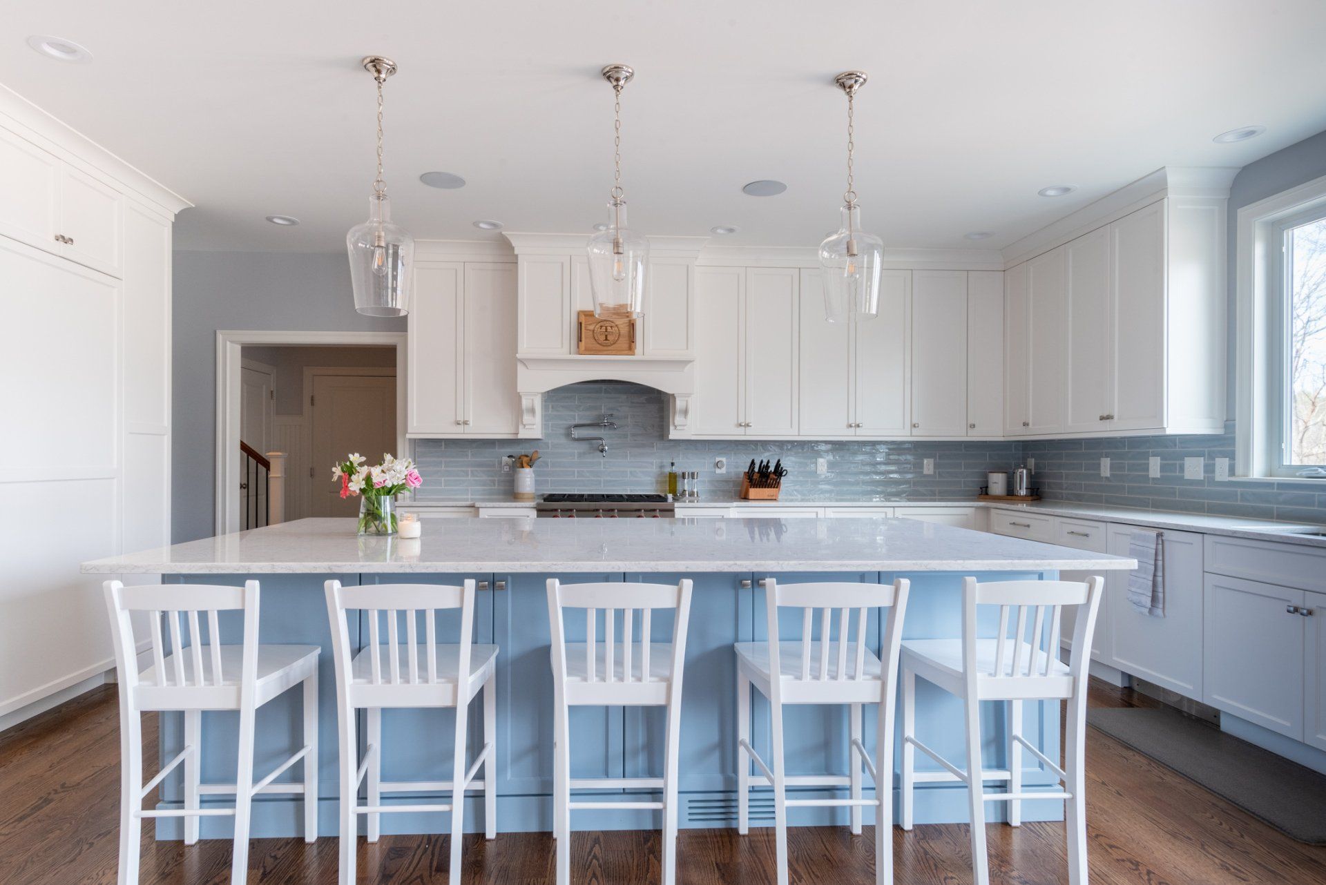 Bright white kitchen with island, pendant lights, gray backsplash, and bar stools