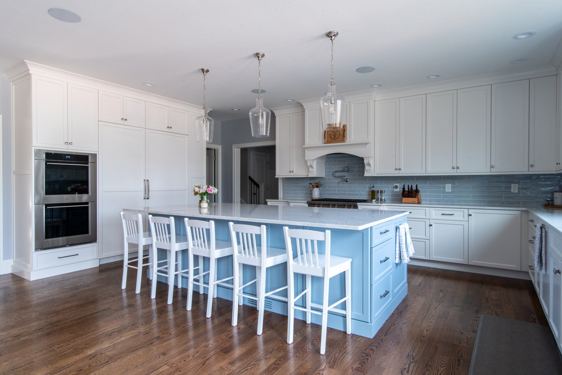 Bright modern kitchen with white cabinets, blue island, hardwood floors, and barstools
