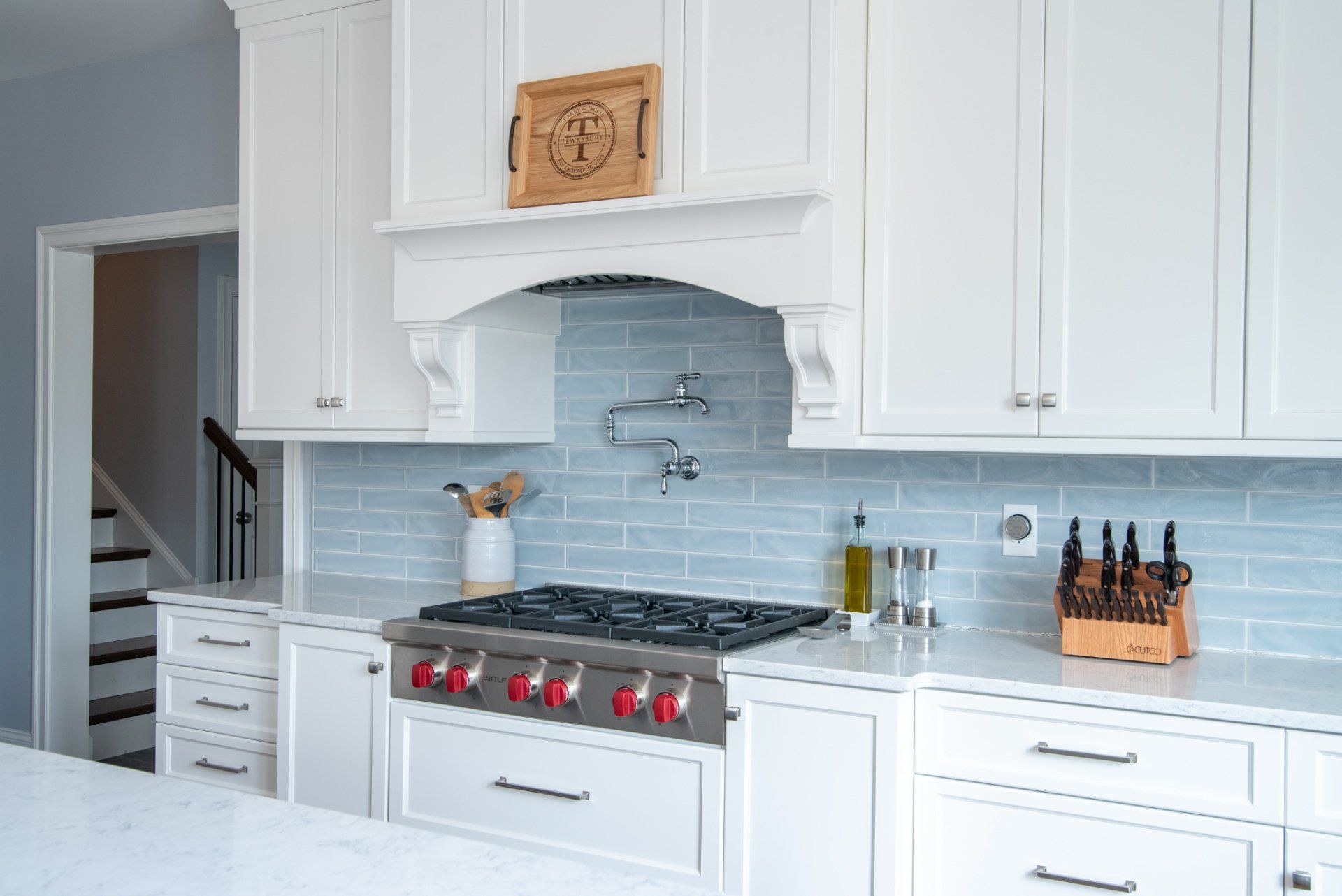 Bright white kitchen with blue tile backsplash, stainless stove, and built-in cabinets
