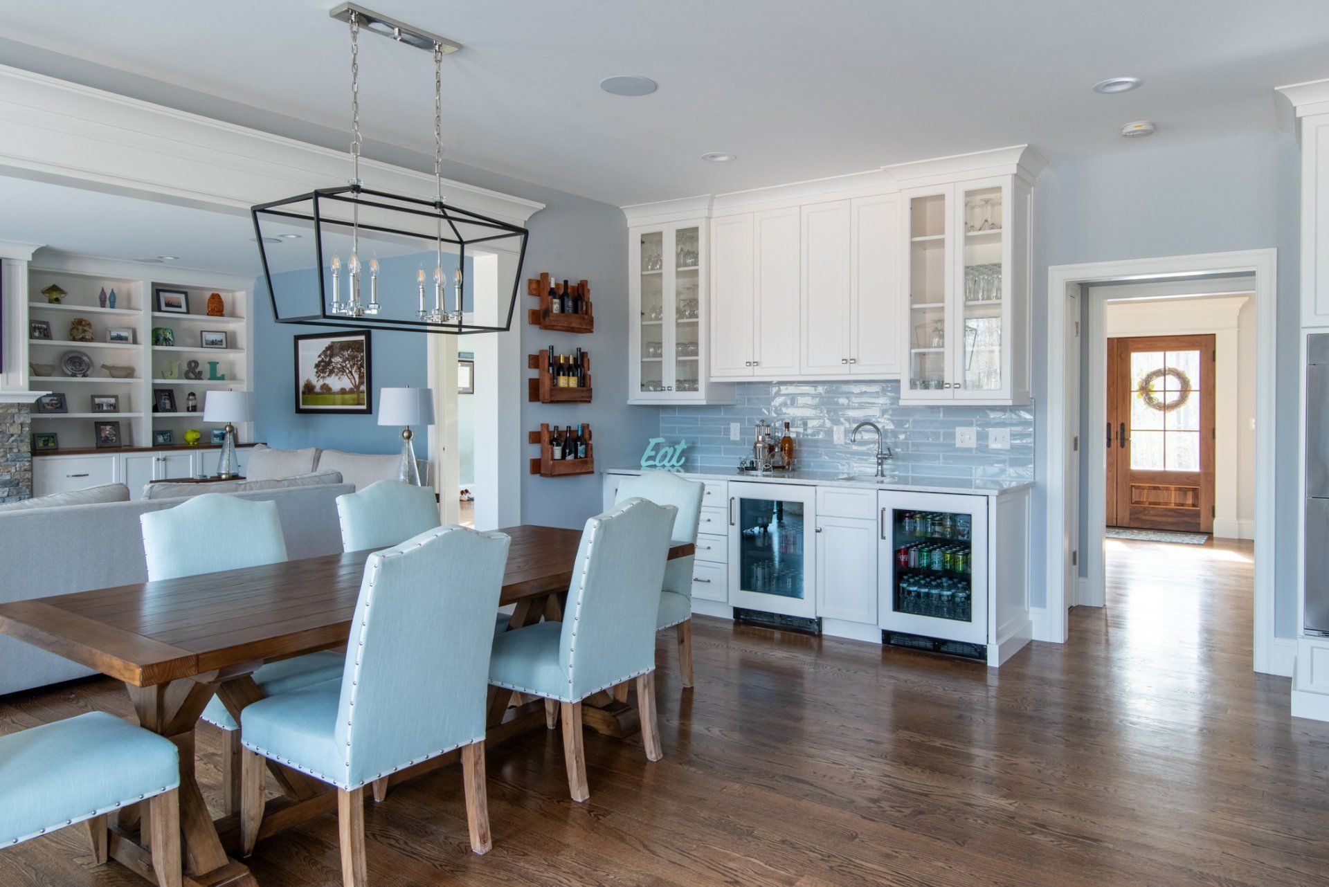 Bright open dining area with a wooden table, blue chairs, white cabinets, and hardwood floors
