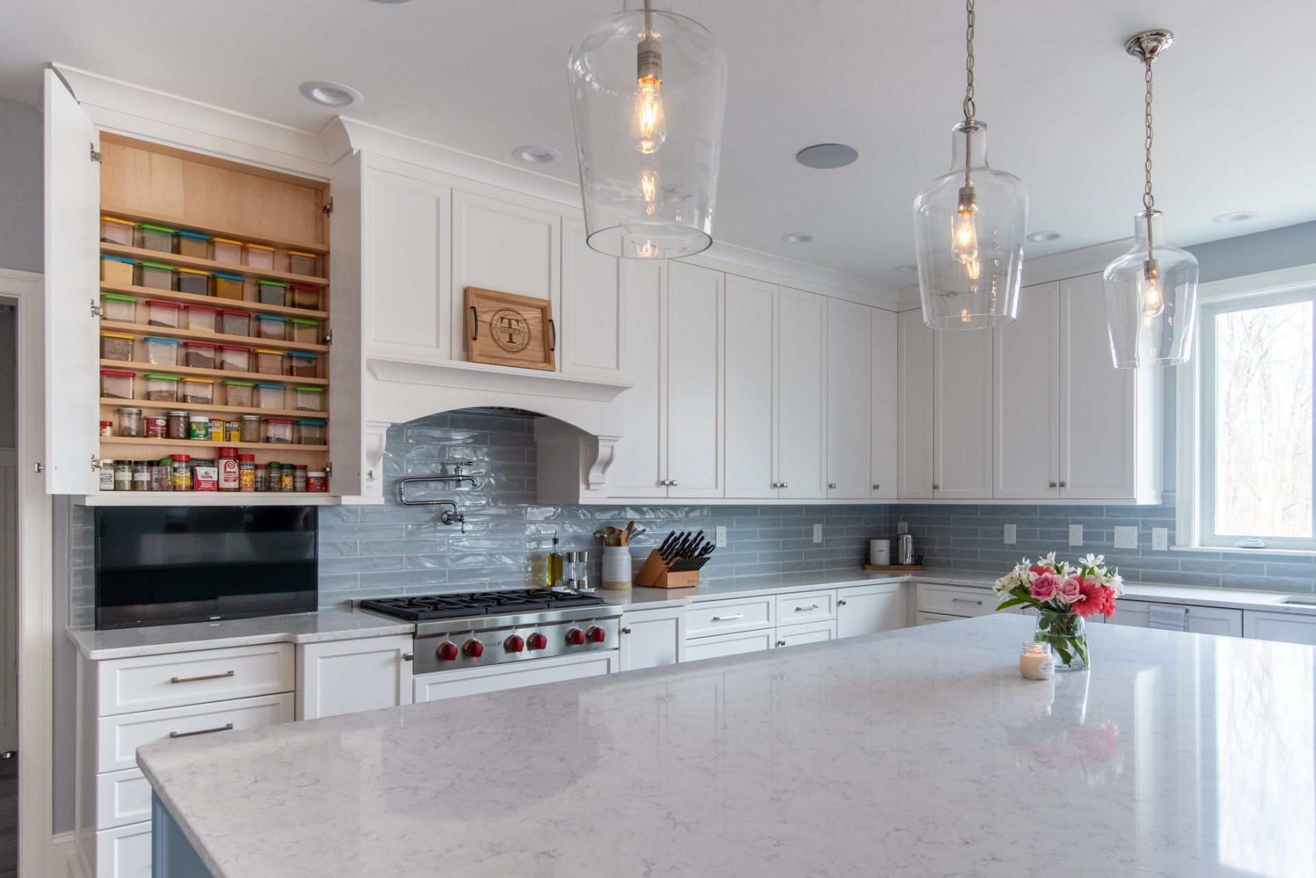 Bright white kitchen with large island, pendant lights, and built-in pantry shelves