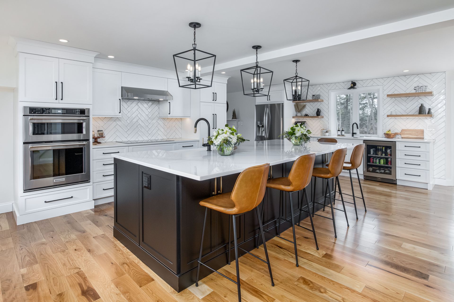 Bright modern kitchen with white cabinets, black island, and three tan barstools on hardwood floors