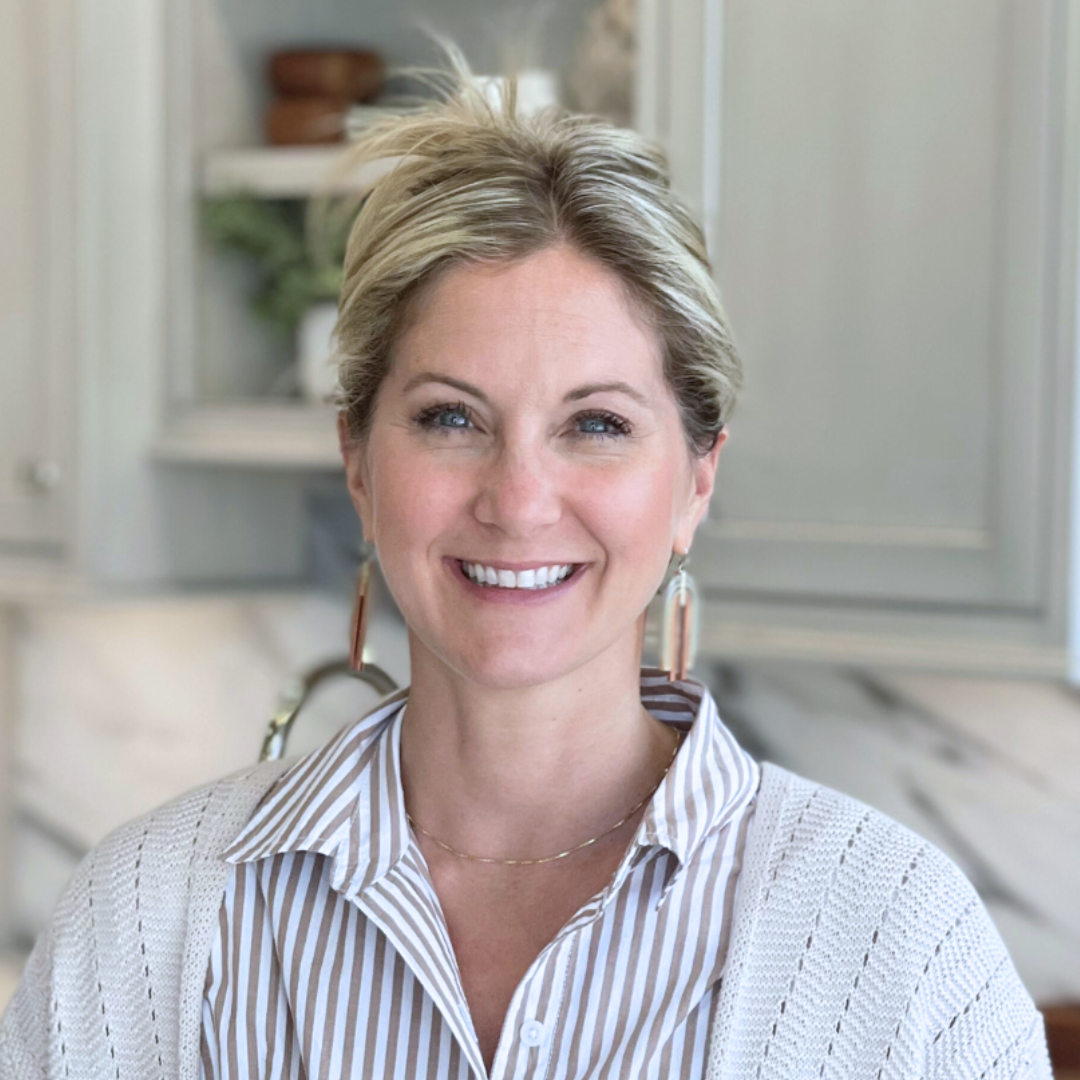 Smiling woman in a striped shirt standing in a bright kitchen with marble countertops