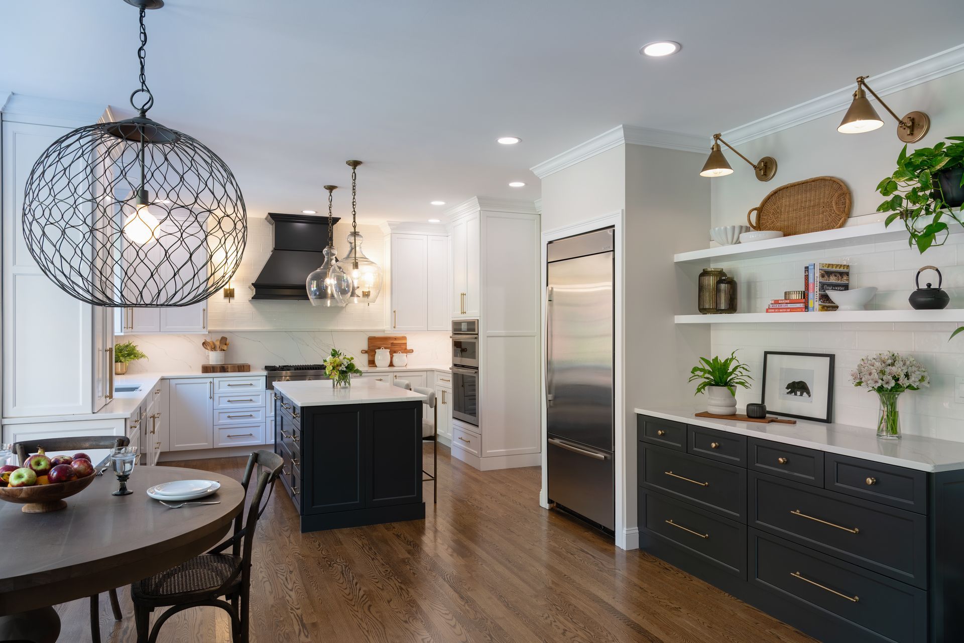 Modern kitchen with dark cabinets, white island, stainless fridge, and dining table with decorative lighting