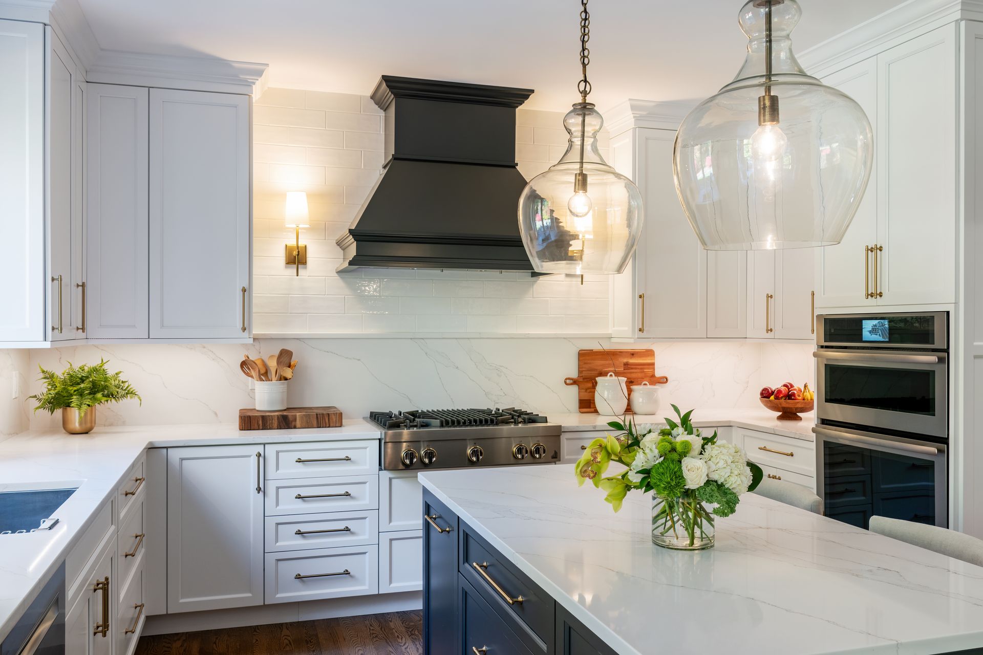Bright modern kitchen with white cabinets, marble island, black range hood, and pendant lights