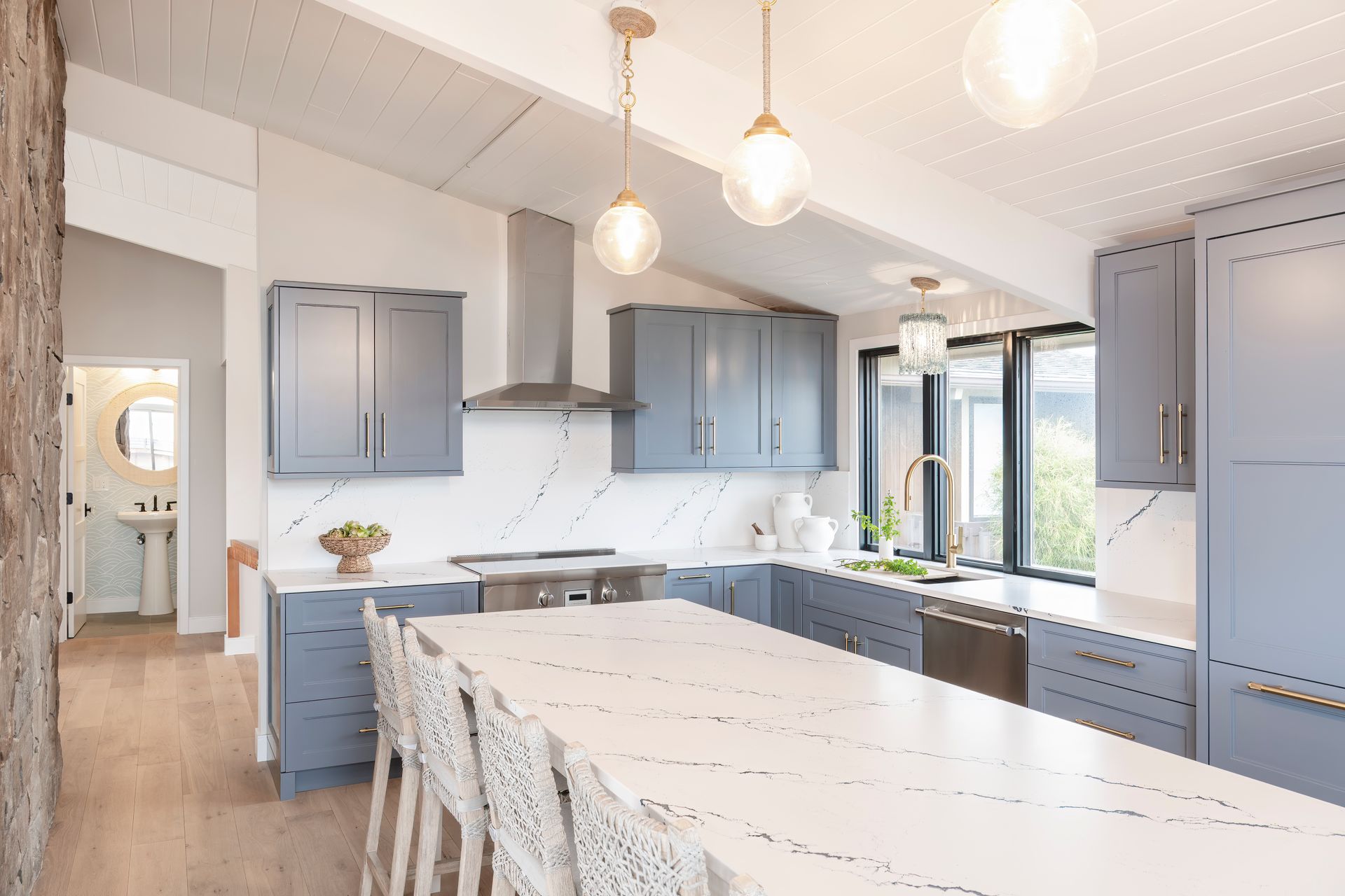 Bright modern kitchen with blue cabinets, white island, pendant lights, and a window by the sink