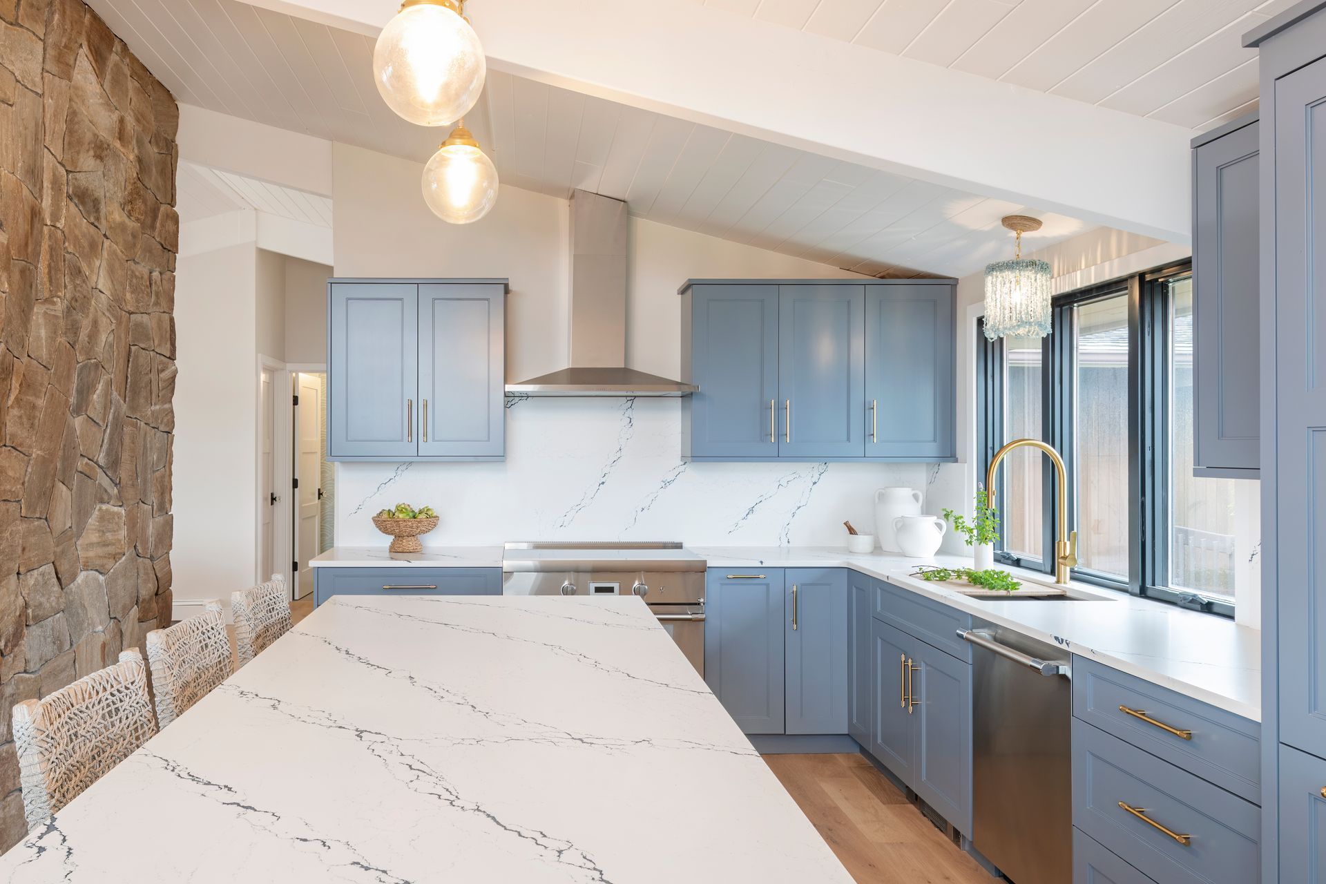 Modern kitchen with blue cabinets, marble island, stainless range, and large windows