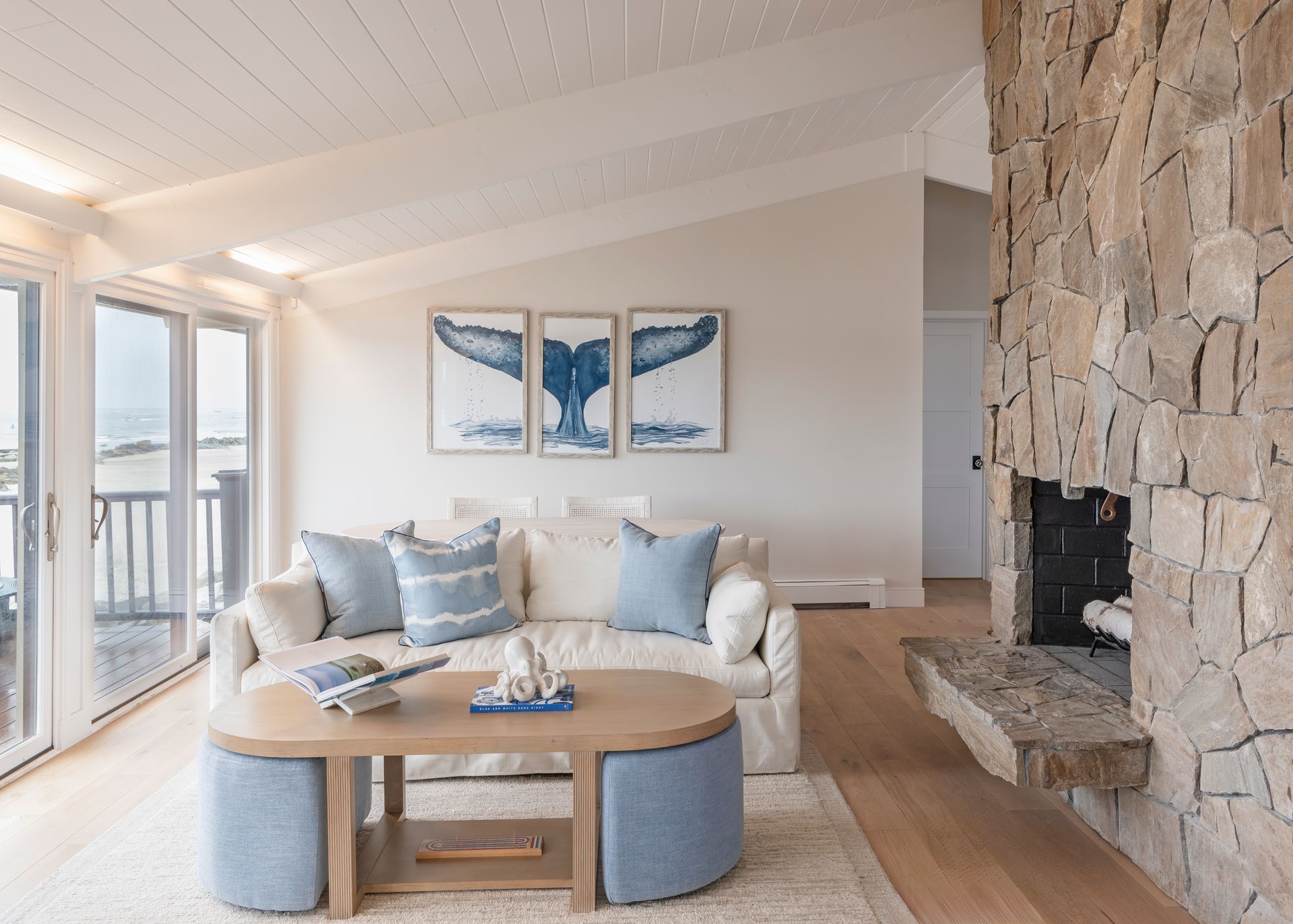 Bright living room with a stone fireplace, white sofa, round coffee table, and ocean-themed wall art.
