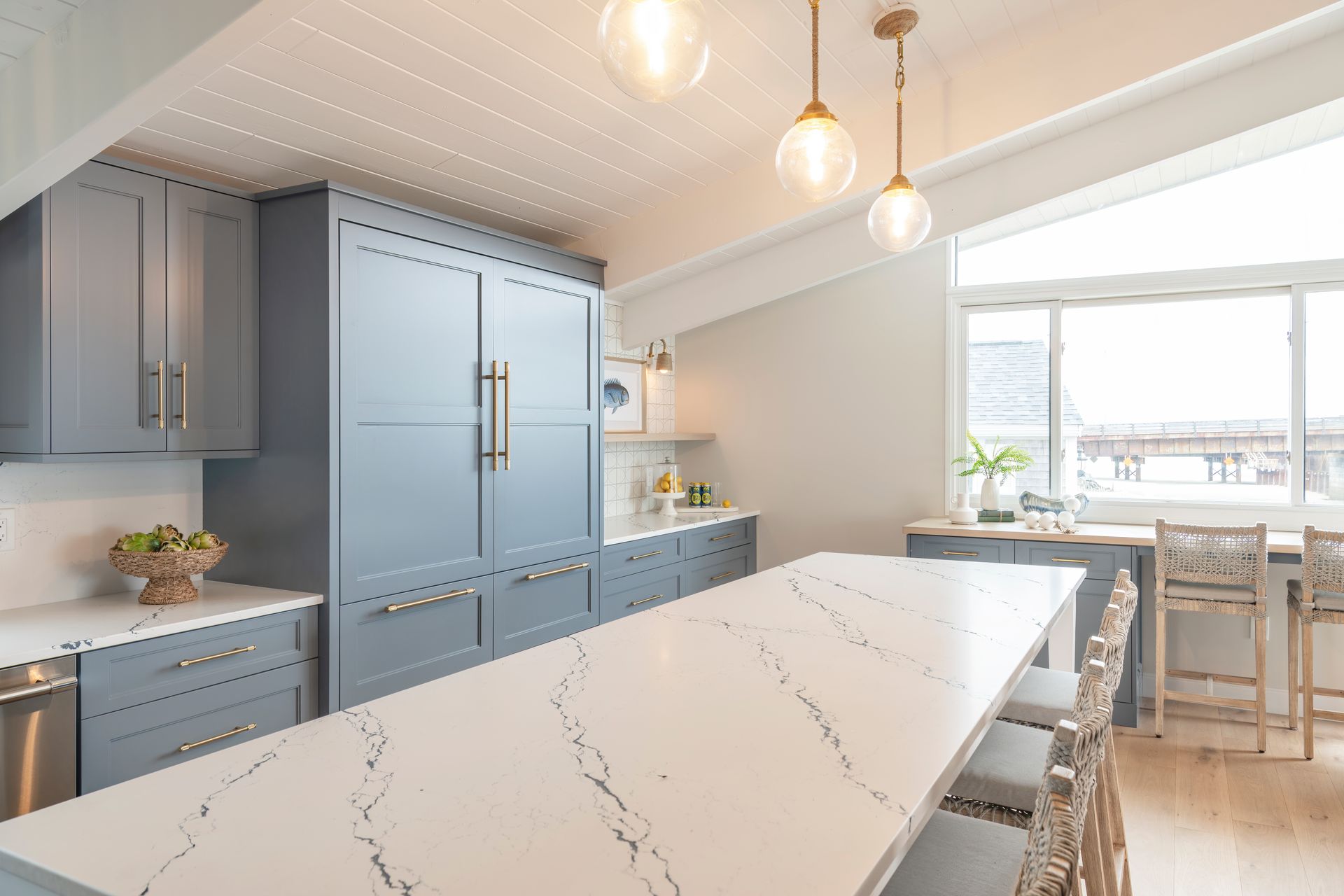 Bright modern kitchen with blue cabinets, white marble island, pendant lights, and a dining nook by the window
