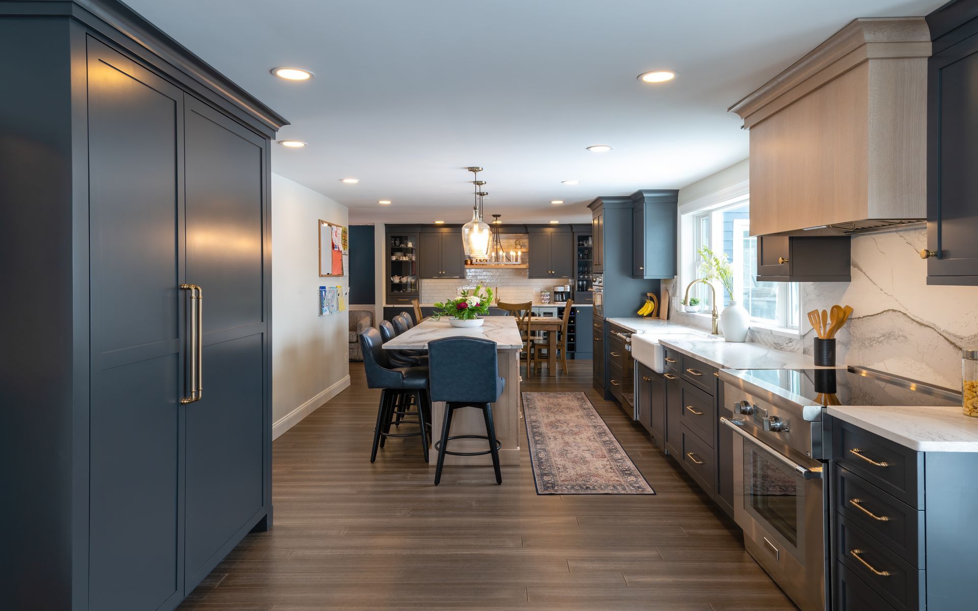 Modern kitchen with blue island, dark cabinets, wood flooring, and dining area by bright windows