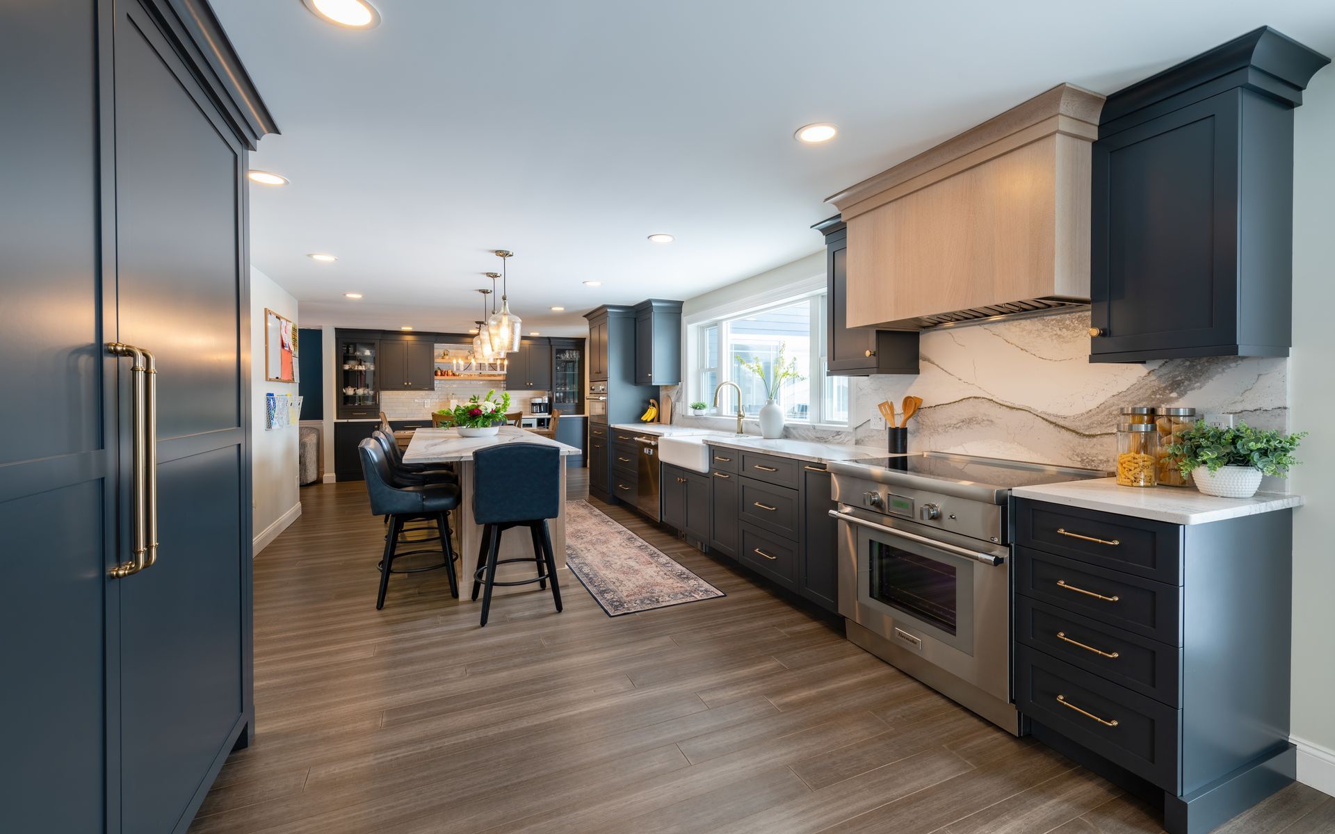 Modern kitchen with dark blue cabinets, light wood island, marble backsplash, and dining area by windows