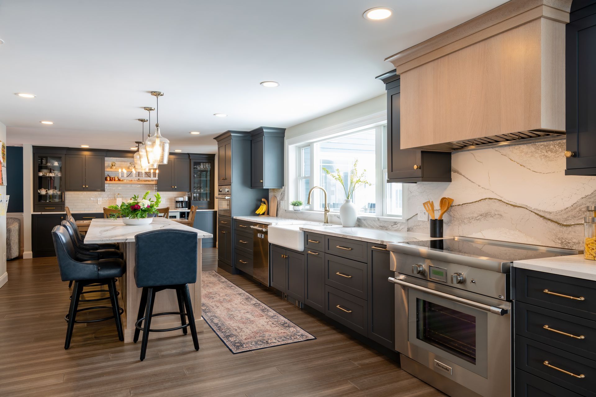 Modern kitchen with dark cabinets, marble counters, stainless appliances, and a blue island with stools