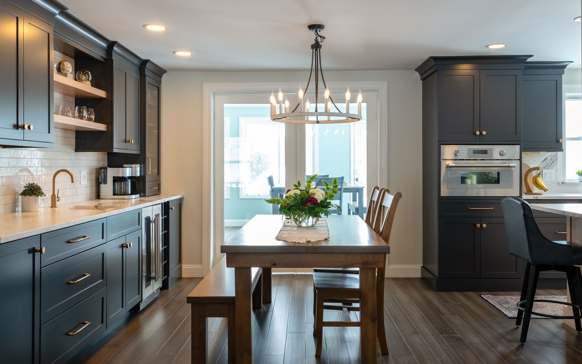 Modern kitchen with navy cabinets, wood island, chandelier, and dining table by bright windows