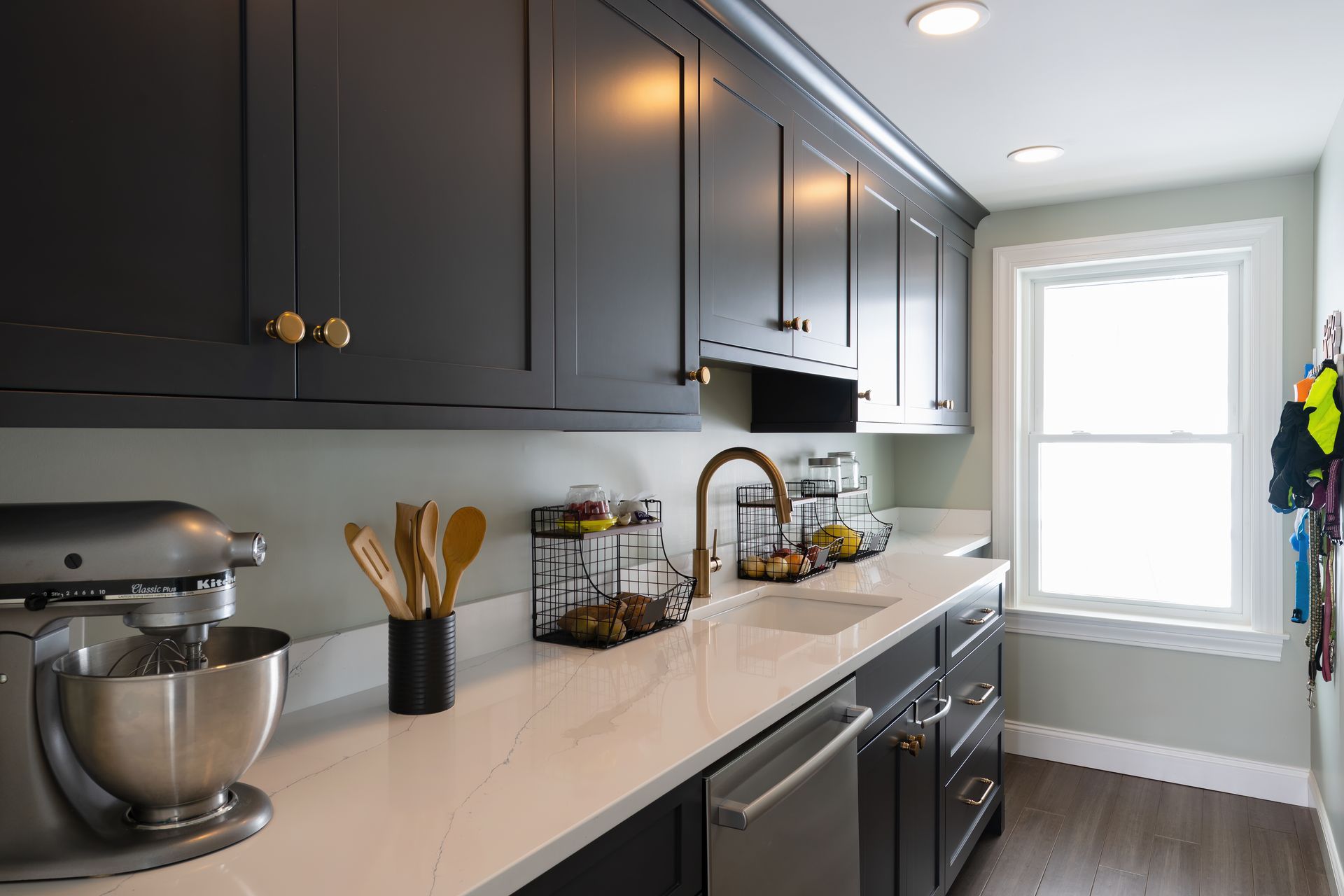 Modern kitchen with dark cabinets, white countertops, stand mixer, and a bright window.