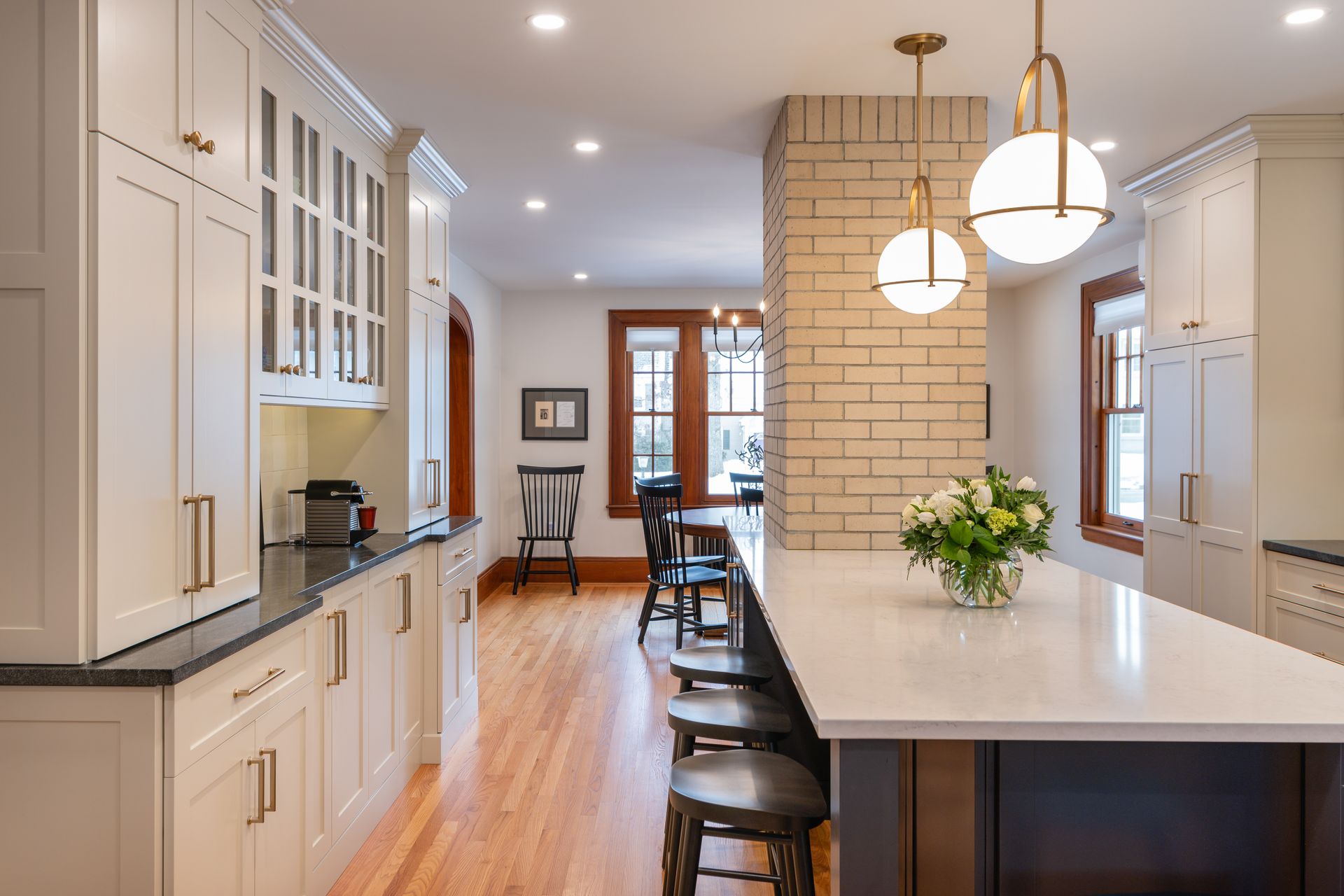 Bright modern kitchen with white cabinets, wood floors, long island, and dining area in the background