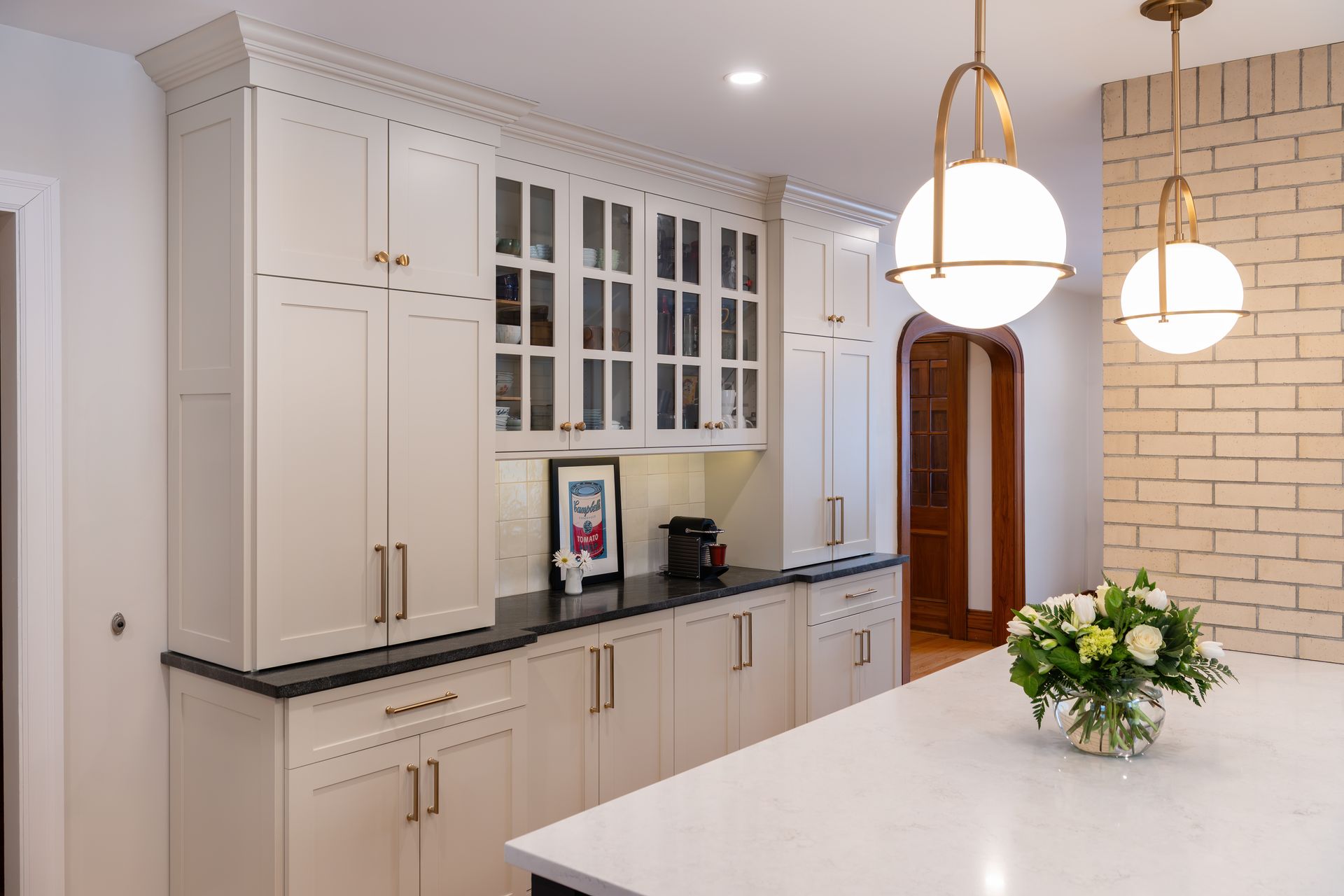 Bright white kitchen with black countertops, glass-front cabinets, and pendant lights over a marble island.
