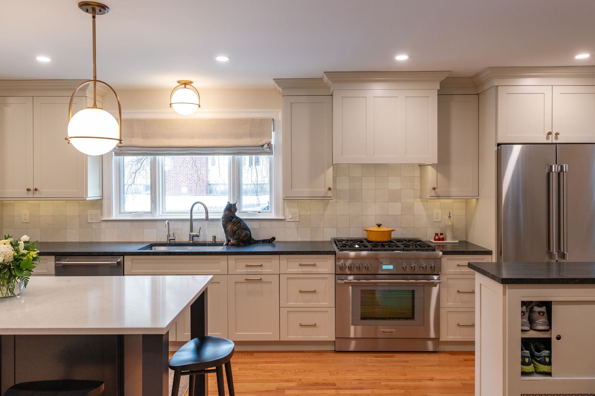 Bright modern kitchen with white cabinets, stainless steel fridge, island, and window over the sink