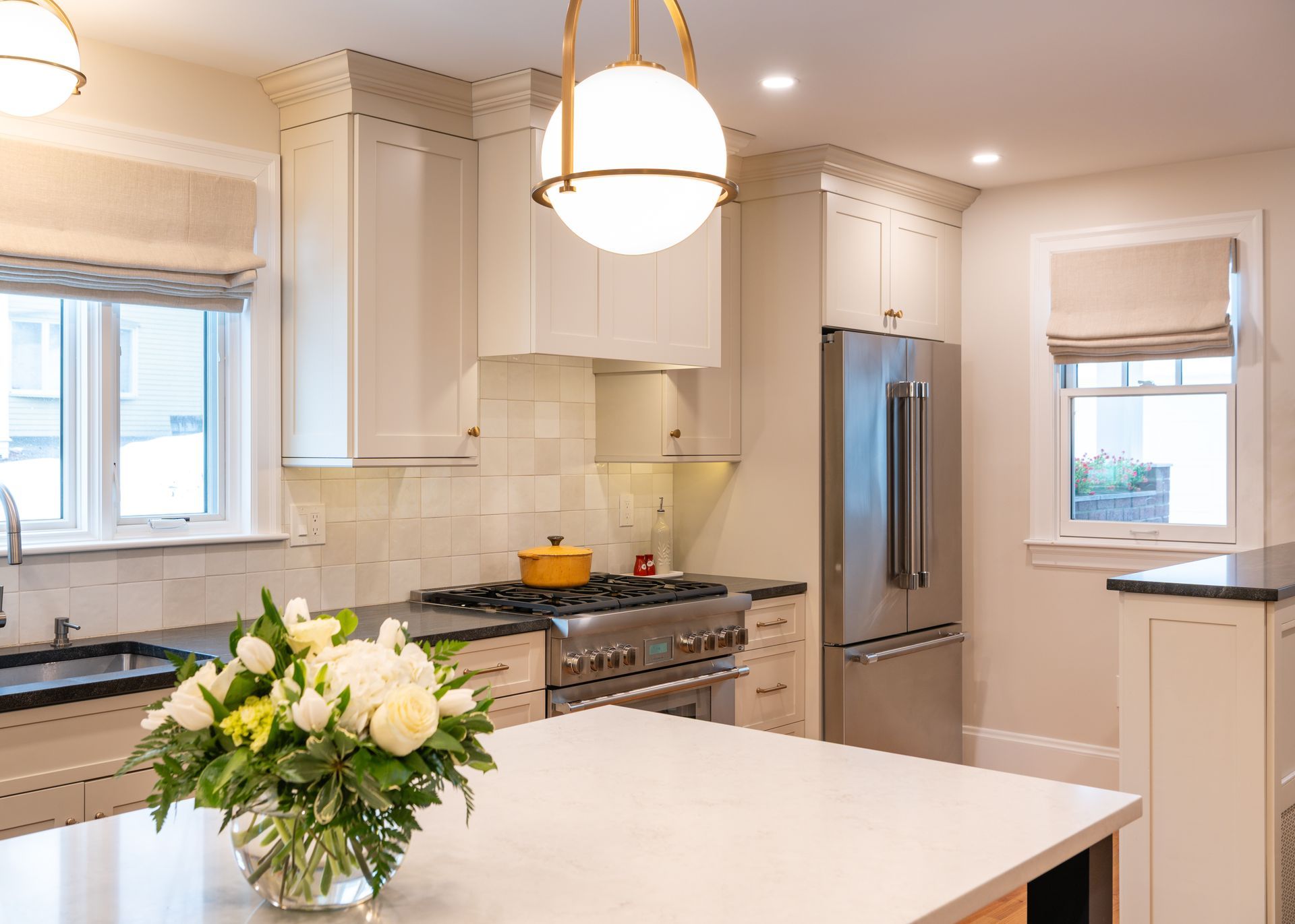 Bright modern kitchen with white cabinets, stainless steel fridge, island, and a vase of flowers in the foreground