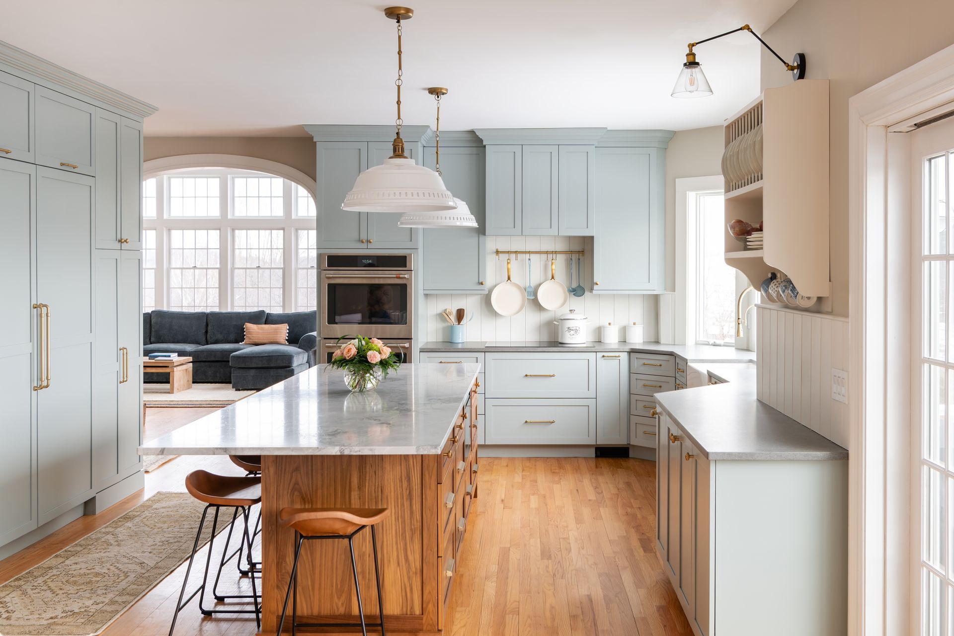 Bright kitchen with pale blue cabinets, wood island, marble countertop, and large windows