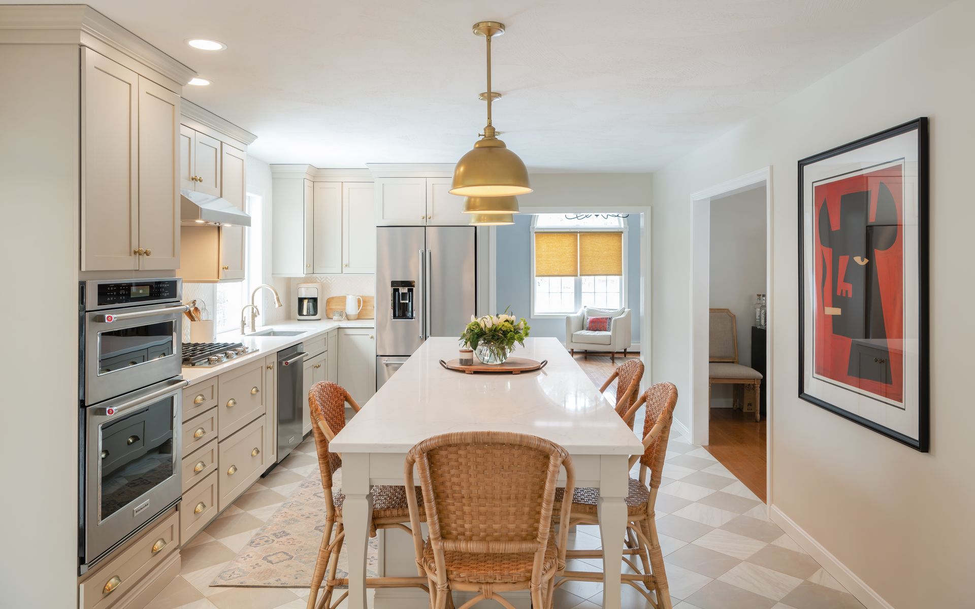 Bright modern kitchen with white cabinets, a dining table, wicker chairs, and a gold pendant light