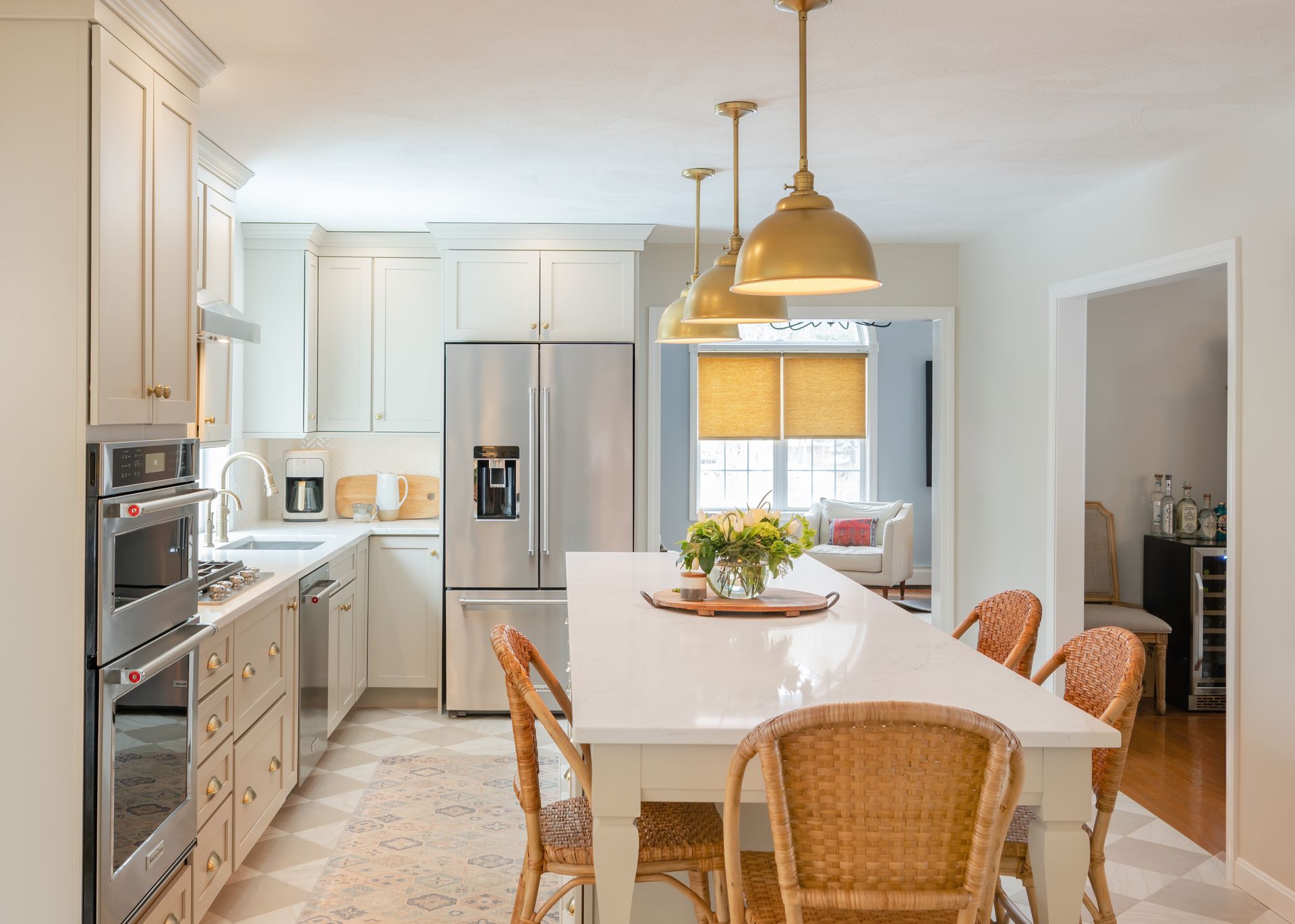 Bright kitchen with white cabinets, stainless fridge, island, wicker chairs, and gold pendant lights
