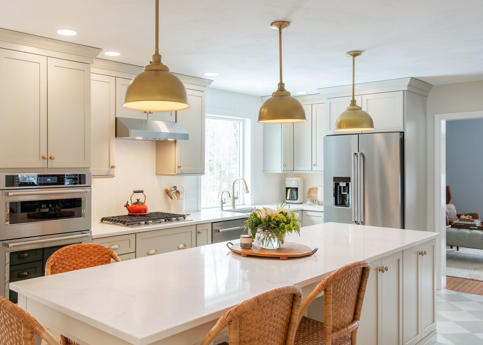 Bright white kitchen with island, wicker stools, gold pendant lights, and stainless steel fridge