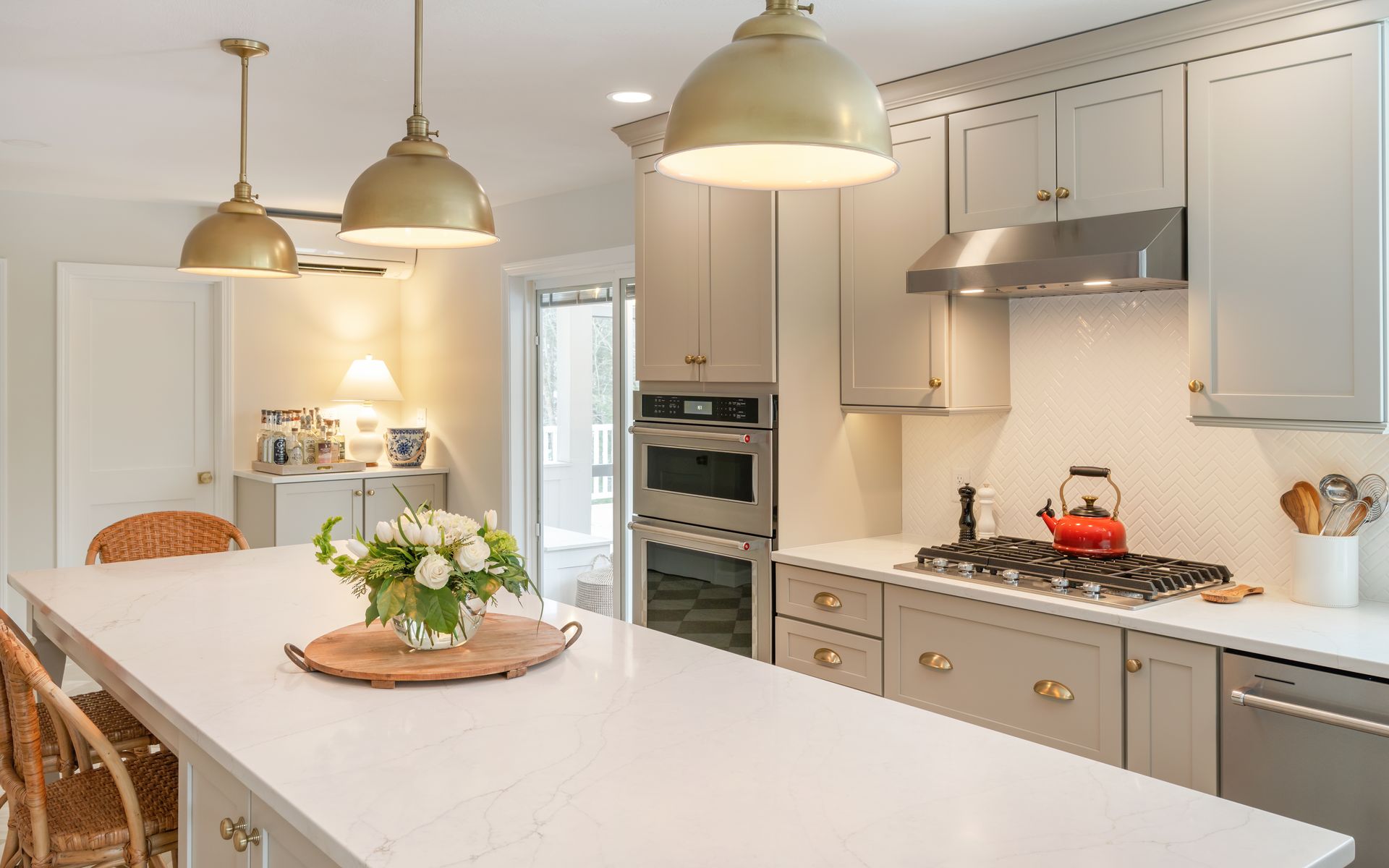 Bright modern kitchen with white island, beige cabinets, brass pendants, and a vase of flowers
