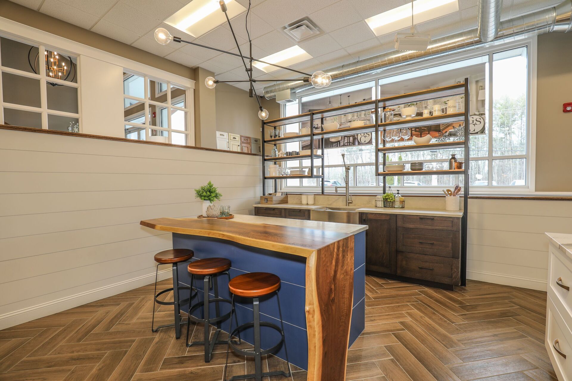 Modern café interior with wooden island table, stools, shelves, and large windows