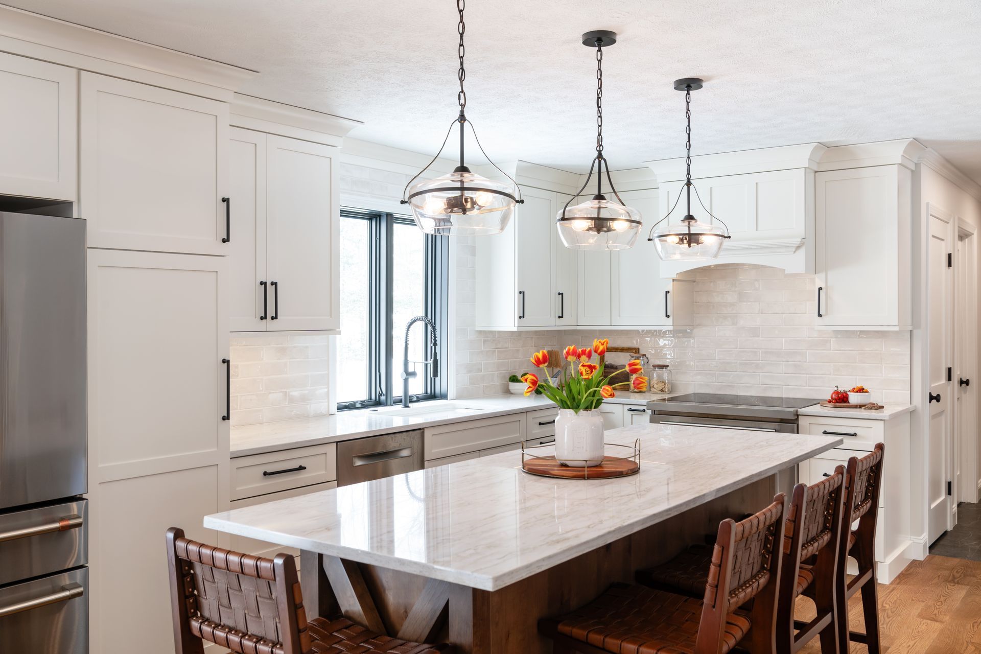Bright modern white kitchen with marble island, pendant lights, and wooden bar stools