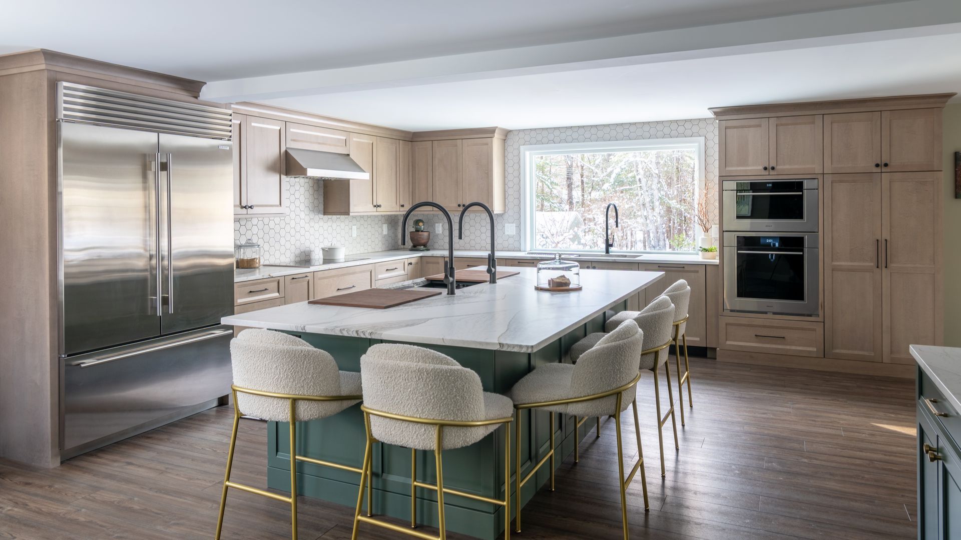 Modern kitchen with a large island, upholstered stools, stainless fridge, and bright window over the sink