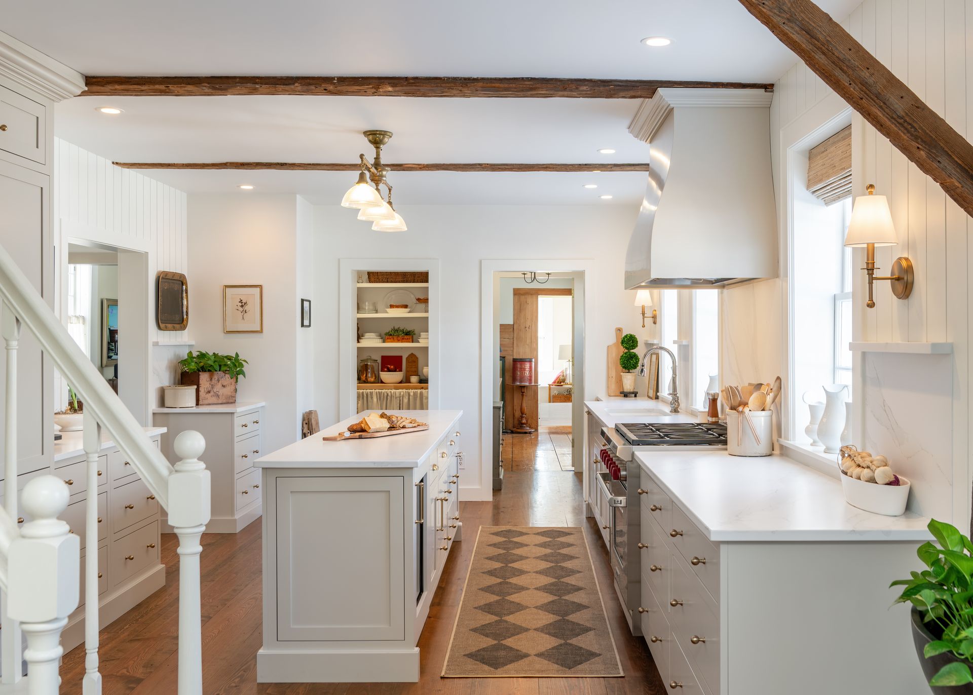 Bright white kitchen with island, pendant lights, wood beams, and a patterned runner leading to a back doorway