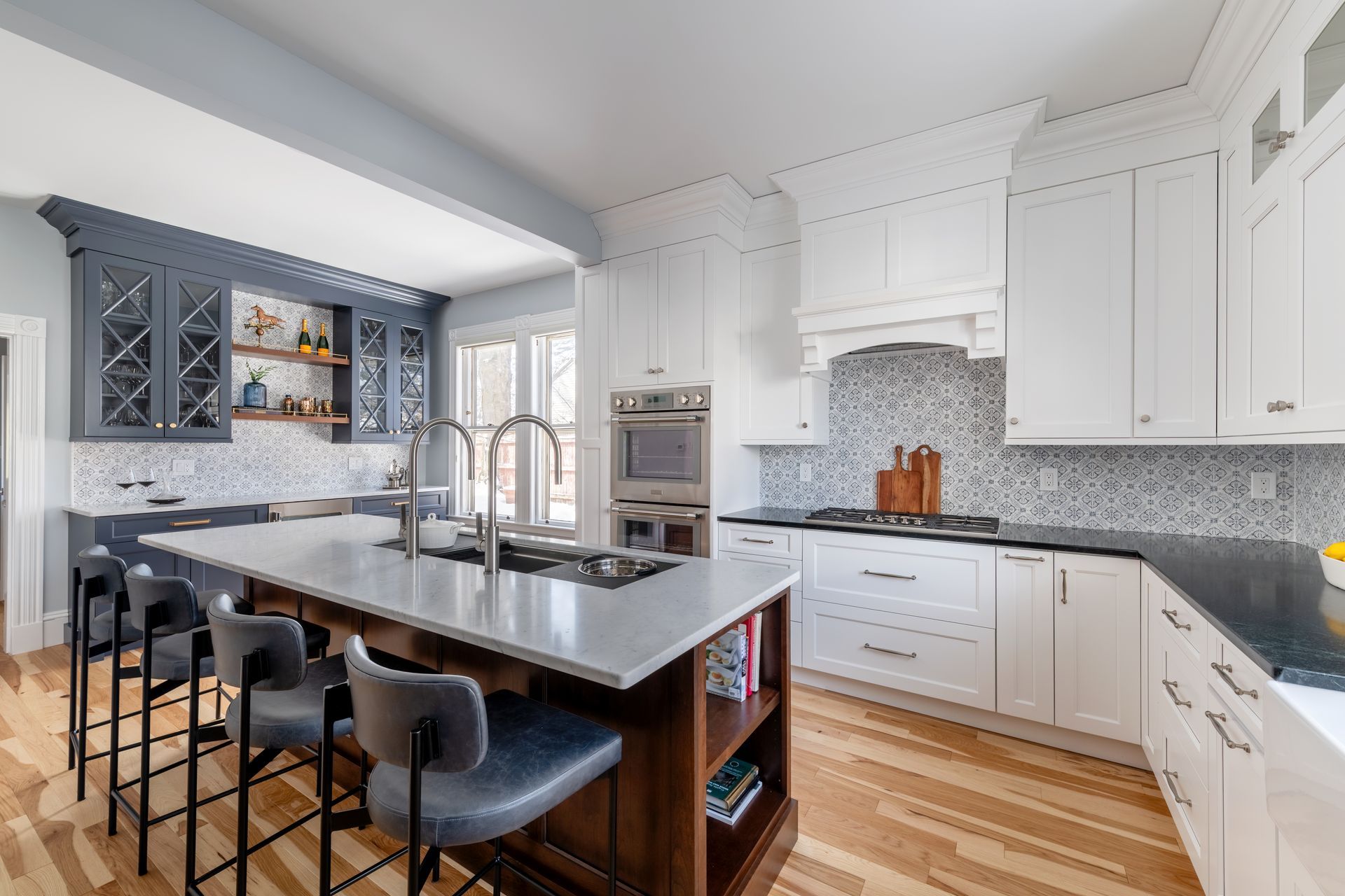 Modern white kitchen with island, dark stools, and blue-gray tile backsplash
