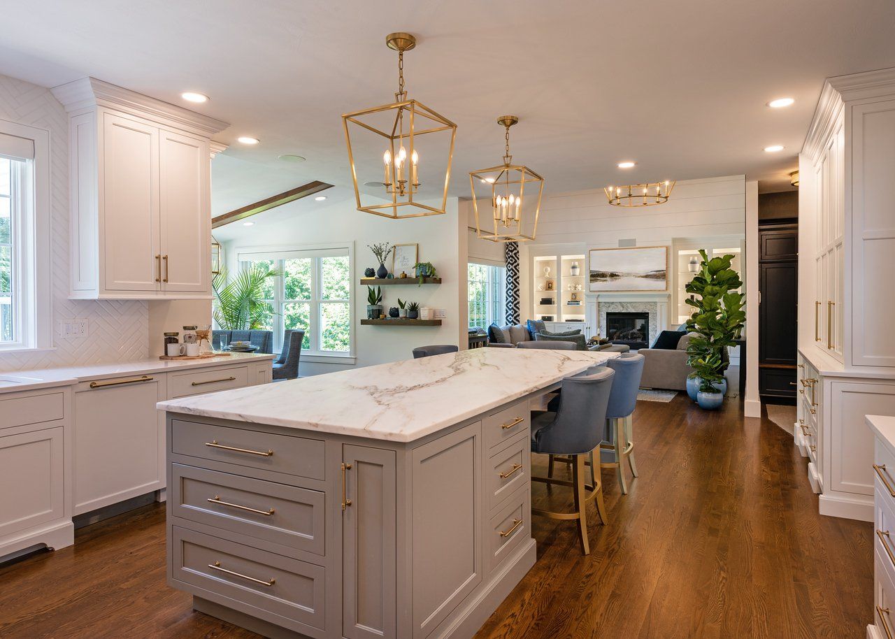 Bright modern kitchen with a large island, white cabinets, wood floors, and gold pendant lights