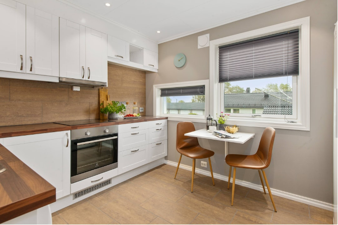Modern kitchen nook with white cabinets, wood accents, and a small table by the window.