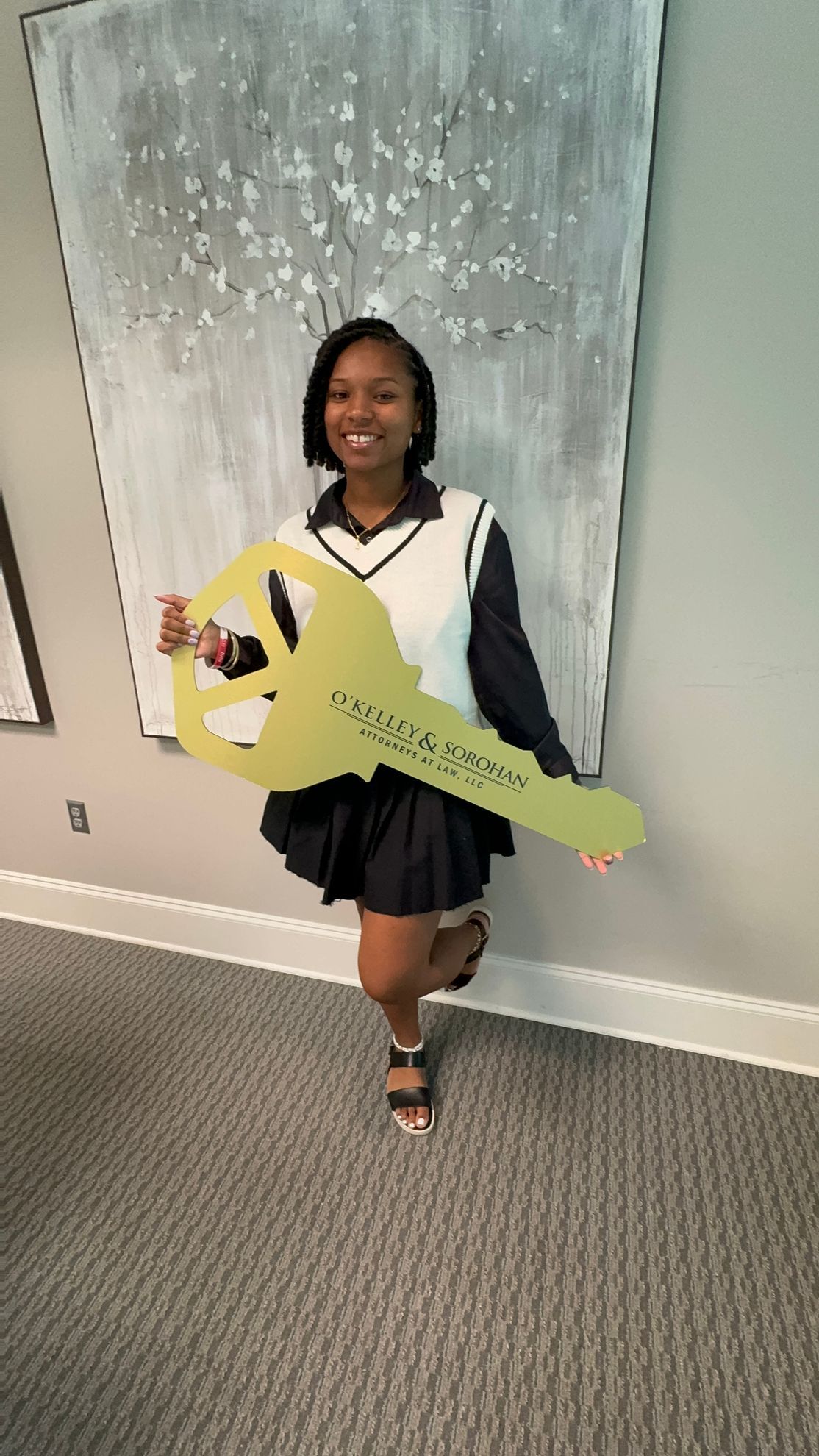 Woman holding oversized gold key in front of artwork; celebratory smile.
