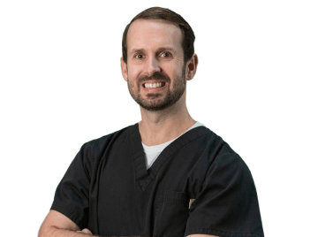 A man in a black scrub is smiling with his arms crossed