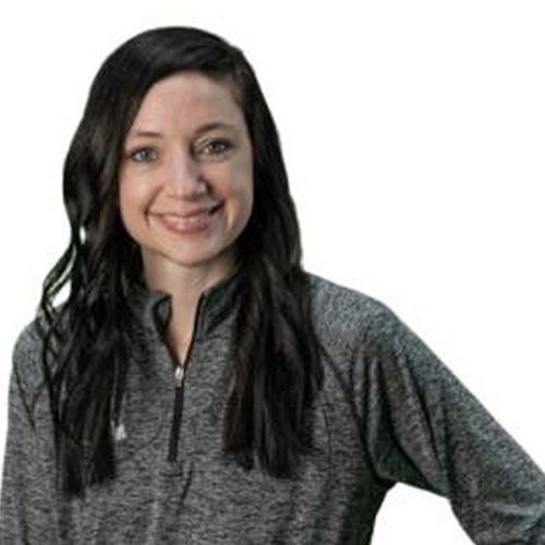 A woman with long dark hair is wearing a gray sweater and smiling.