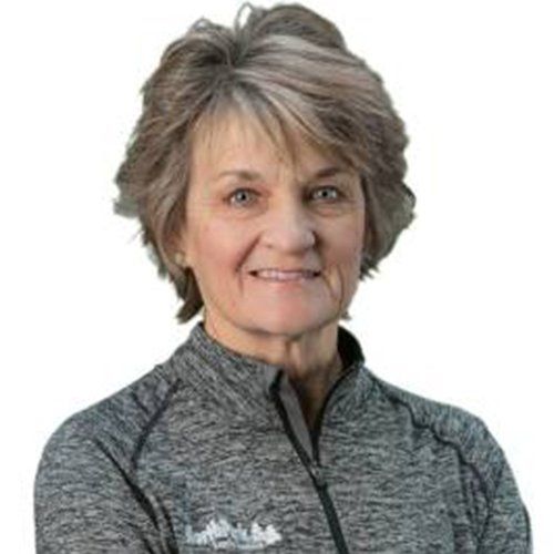 A woman is wearing a gray shirt and smiling with her arms crossed.