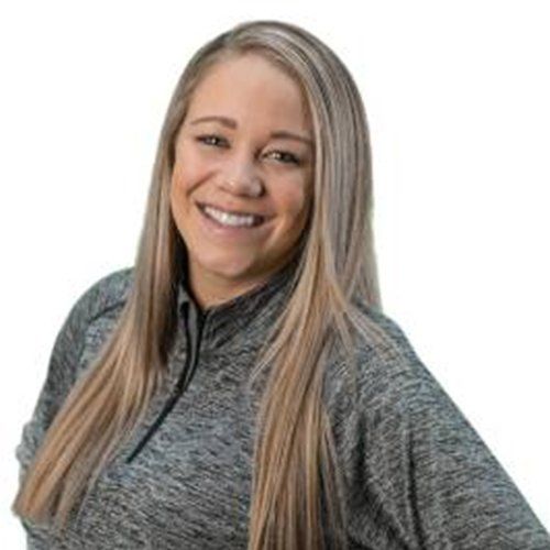 A woman with long blonde hair is wearing a gray shirt and smiling.