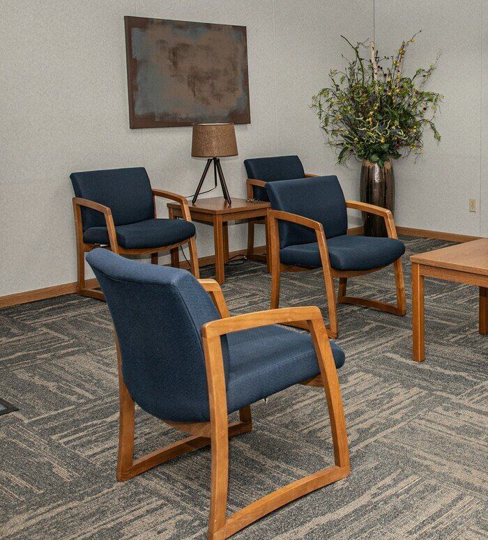 A waiting room with blue chairs and wooden tables