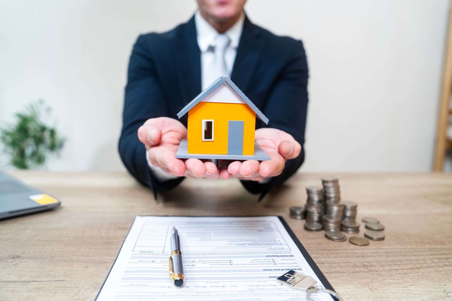 A man in a suit is holding a model house in his hands.