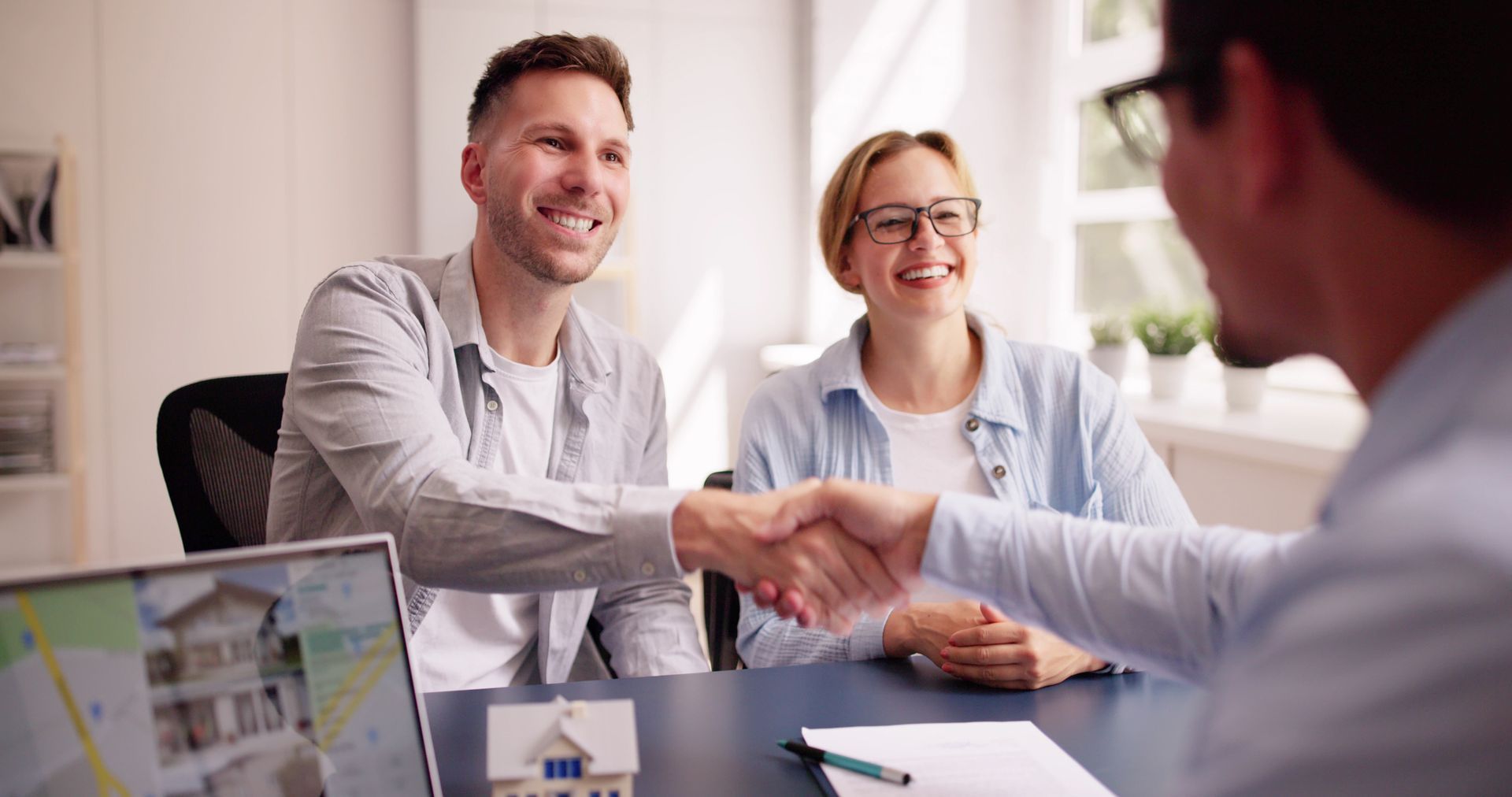 A man and woman are shaking hands with a real estate agent while sitting at a table.