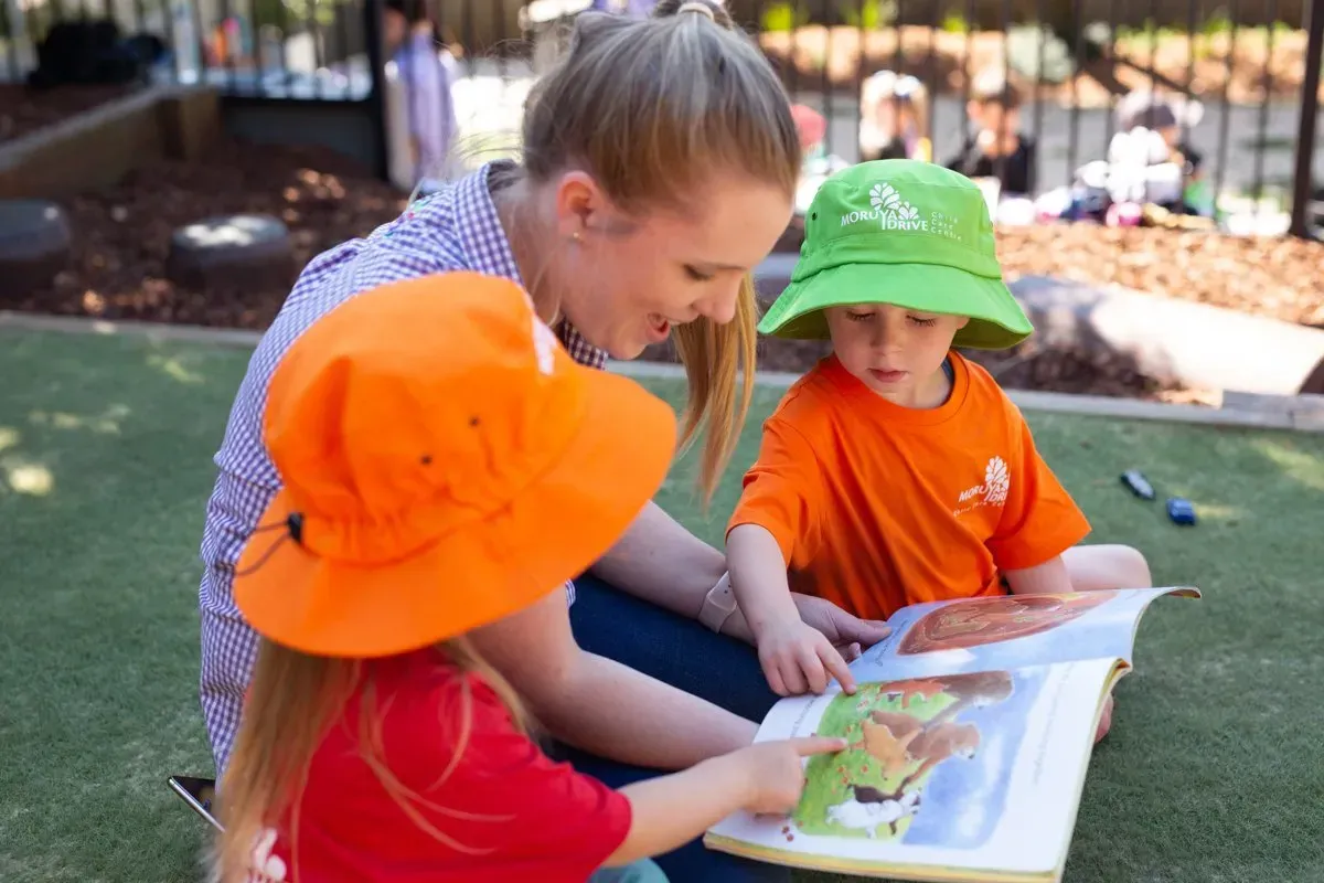 A Woman Is Reading A Book To Two Children — Moruya Drive Child Care Centre In Port Macquarie, NSW