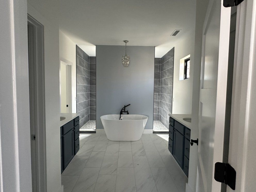 Modern bathroom with a freestanding tub, gray tile walls, and black vanity cabinets