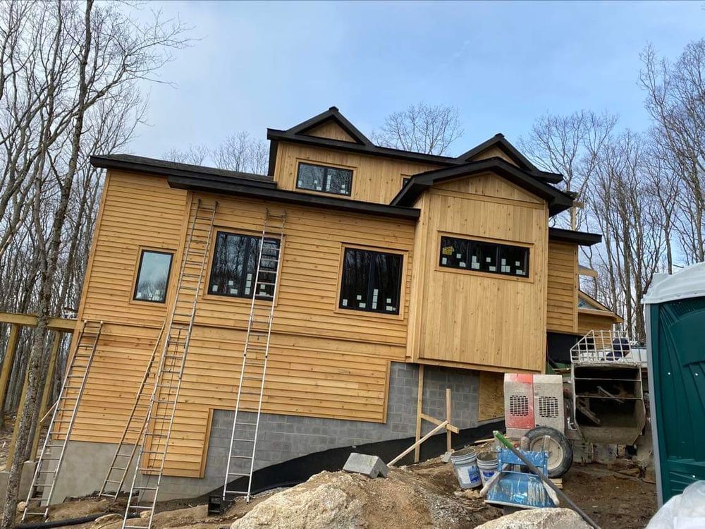 Partially built wooden house with black window frames and construction materials in front