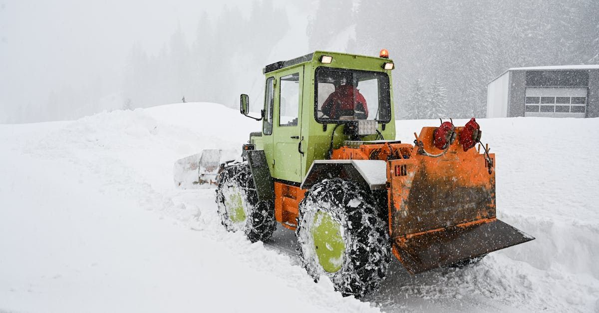 A green and orange tractor is plowing snow on a snowy road.